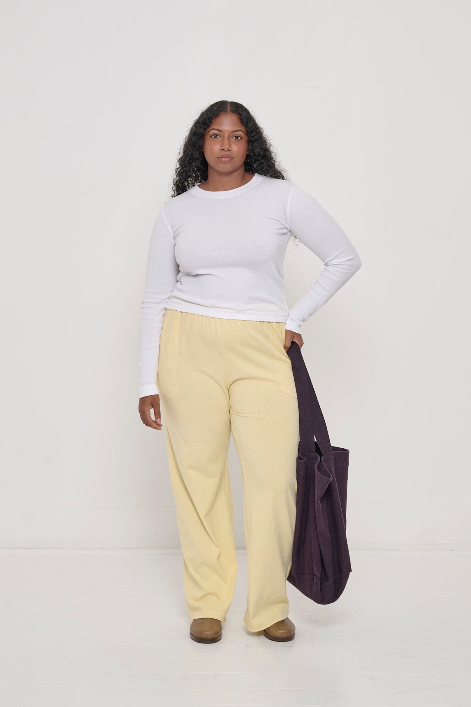 A woman wearing a White Rib Long Sleeve, French Butter Apartment Pants, holding a Mulberry Big Tote against her hip.