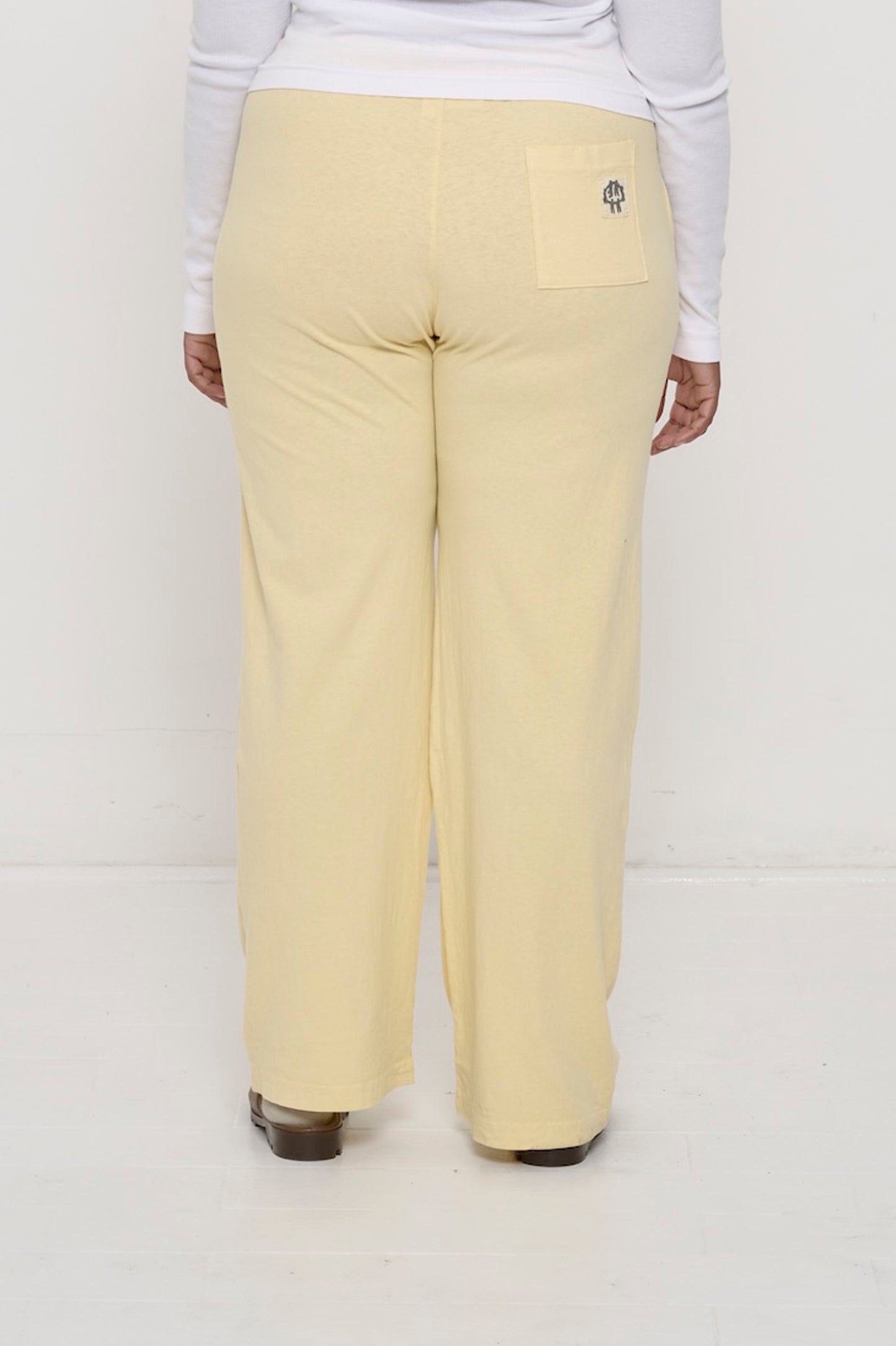 Back view, waist down: a person in French Butter Apartment Pants, the grey E.W logo printed on the right back pocket.