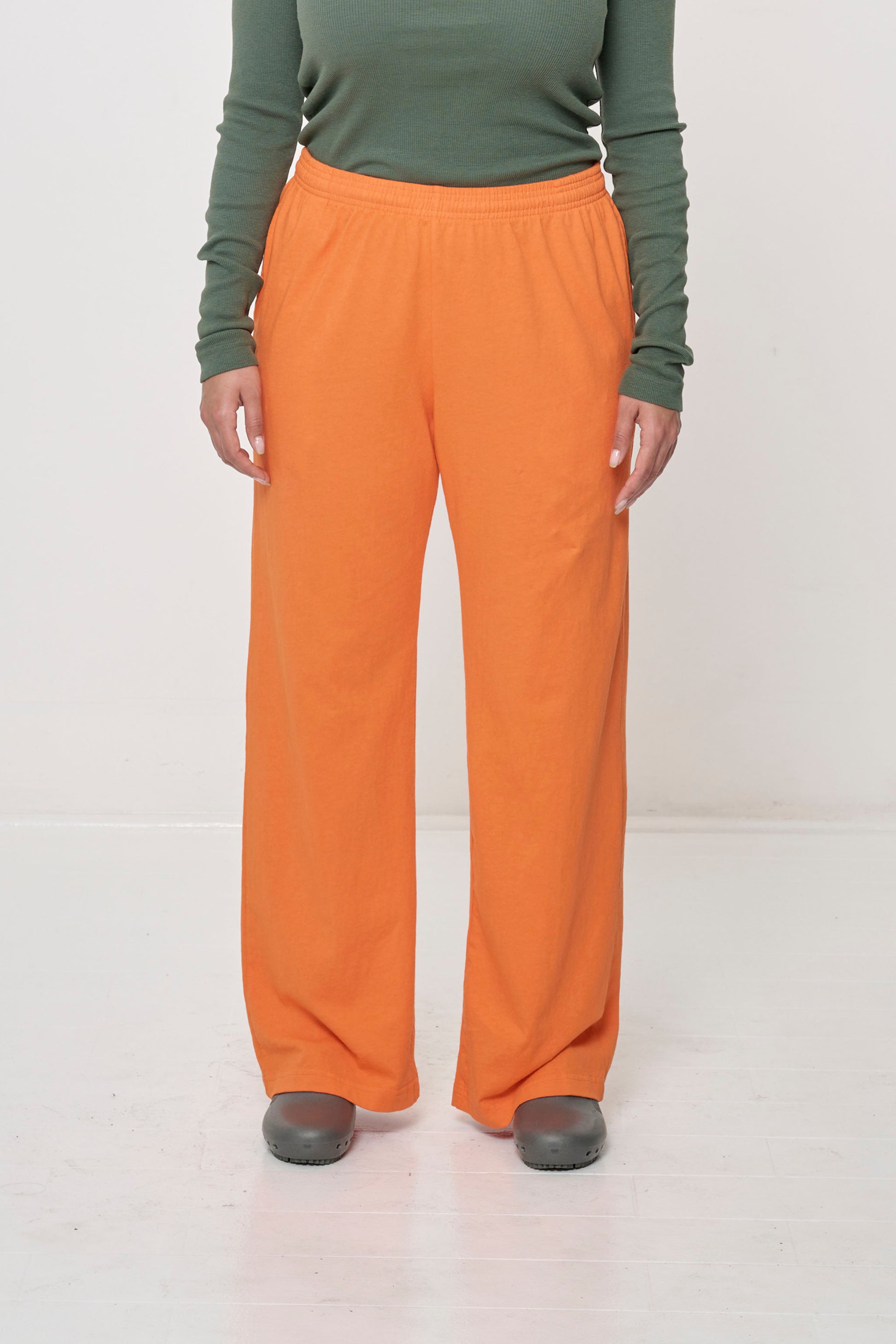 Close-up front view of a person wearing Jerico's Apartment Pants in Persimmon orange, highlighting the elastic waistband and relaxed drape, even when worn with a small amount of ease in the hips.