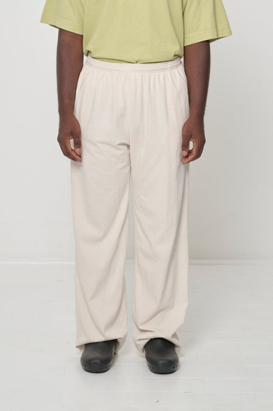 Close-up front view of 5'9" male wearing Jerico's Apartment Pants in Scour (cream) in size L, worn with a moderate amount of ease in the hips and floor skimming hemline.