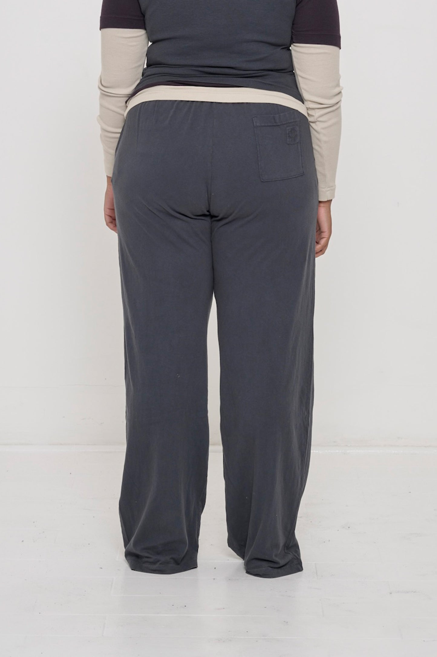 Close-up back view of a person wearing  Apartment Pants in Slate dark grey, showing the E.W logo on the back pocket.