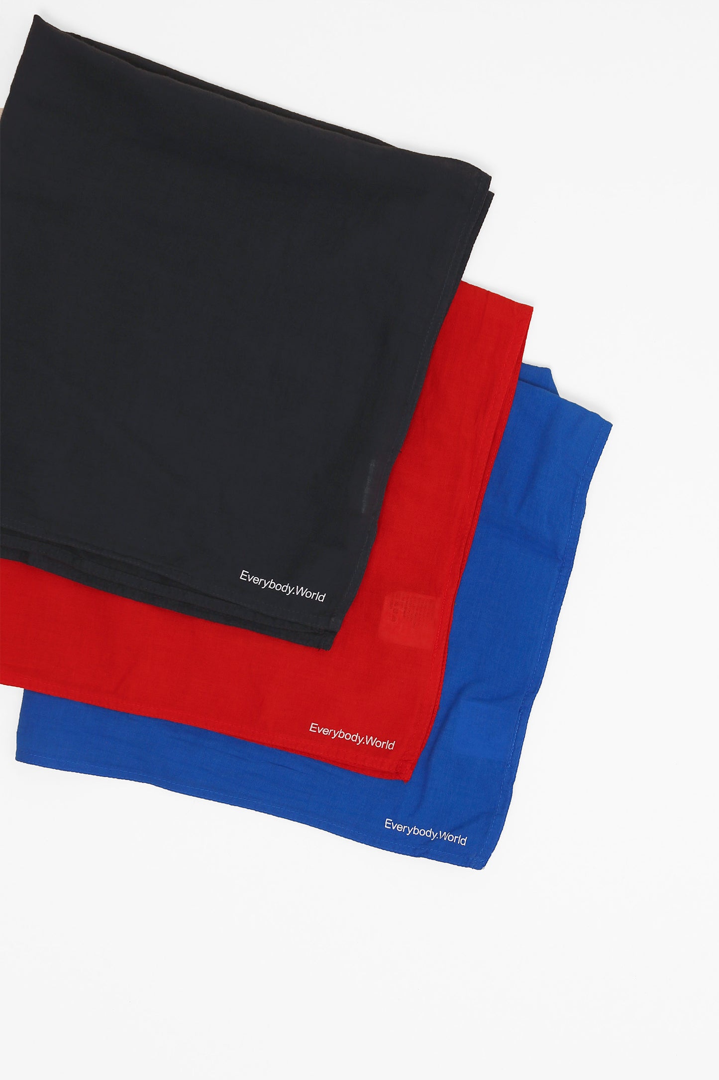 Flat lay of three different colored bandanas, featuring Everybody.World branding on the corners of the bandanas.