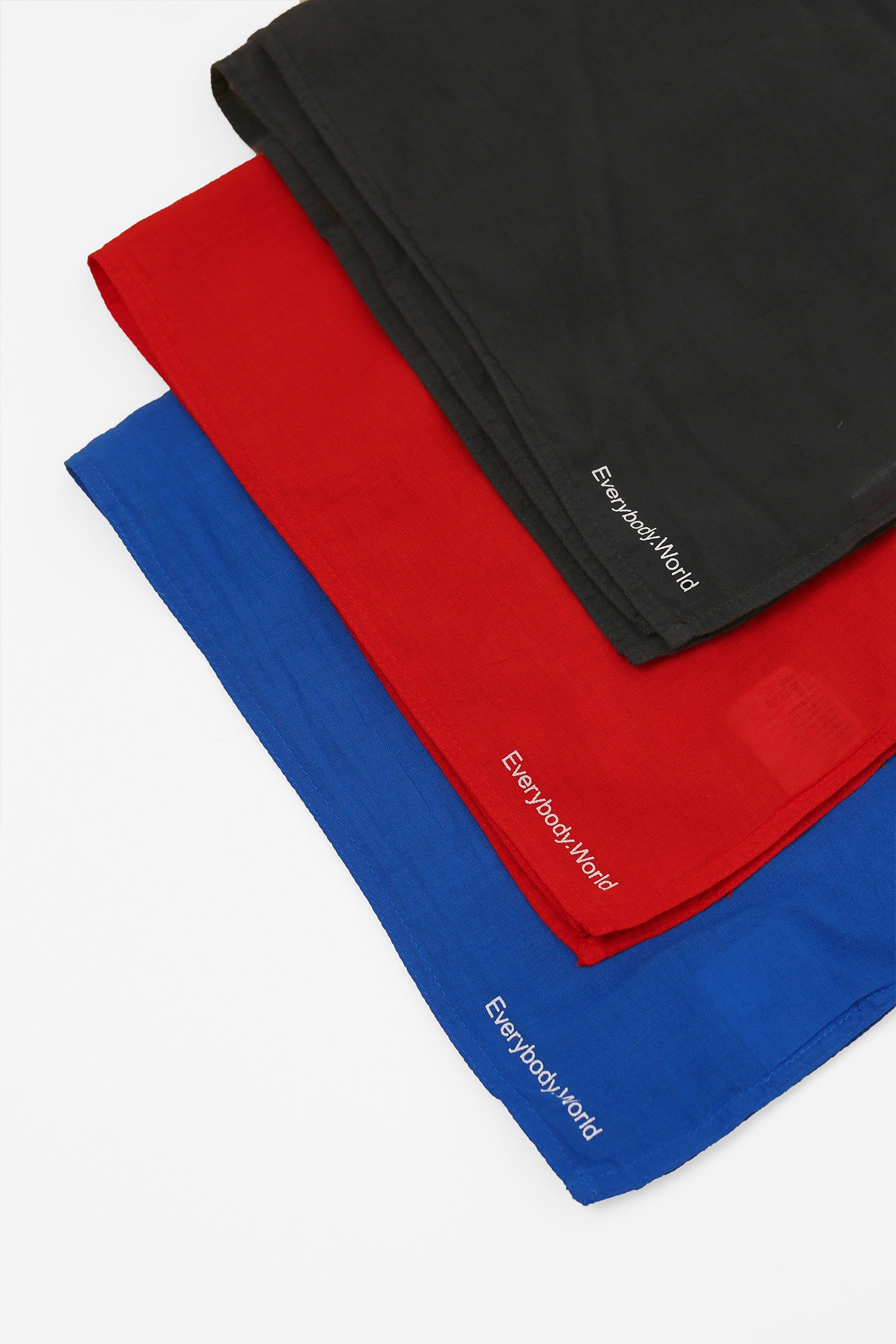Close-up of a flat lay of three different colored bandanas, featuring Everybody.World branding on the corners of the bandanas.