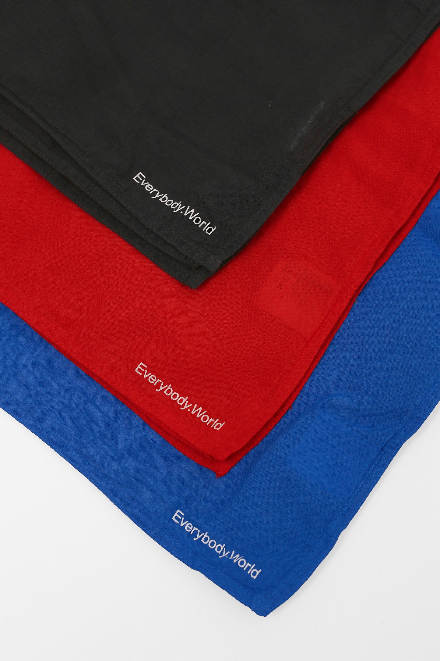 Close-up of a flat lay of three different colored bandanas, featuring Everybody.World branding on the corners of the bandanas.