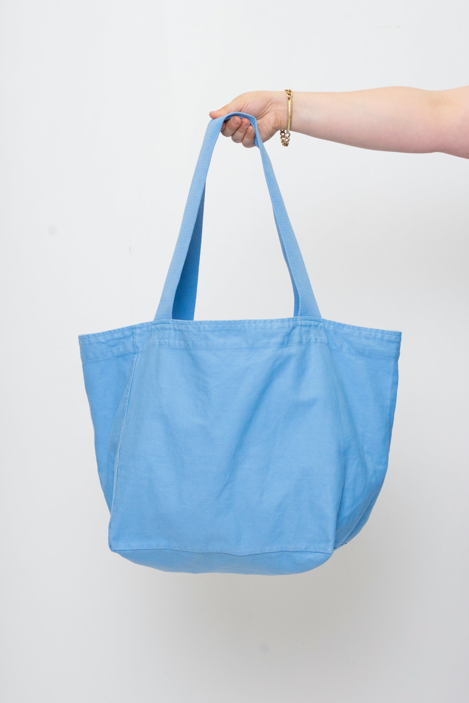 Big Tote in Cielo light blue, held in a person's hand, showing gussets, depth, stitching, and web straps.
