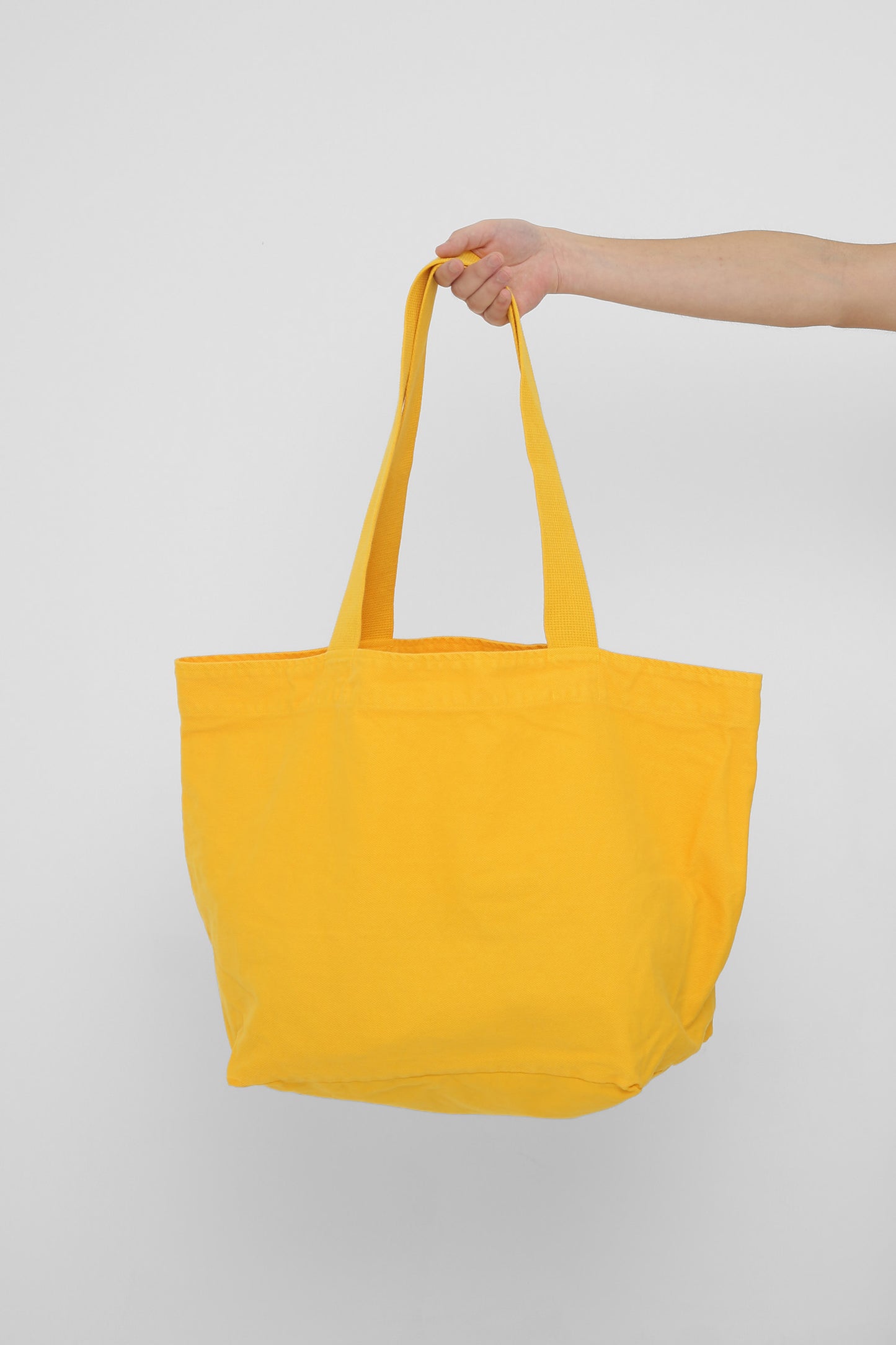 Big Tote in Everybody Yellow, held in a person's hand, showing gussets, depth and stitching.