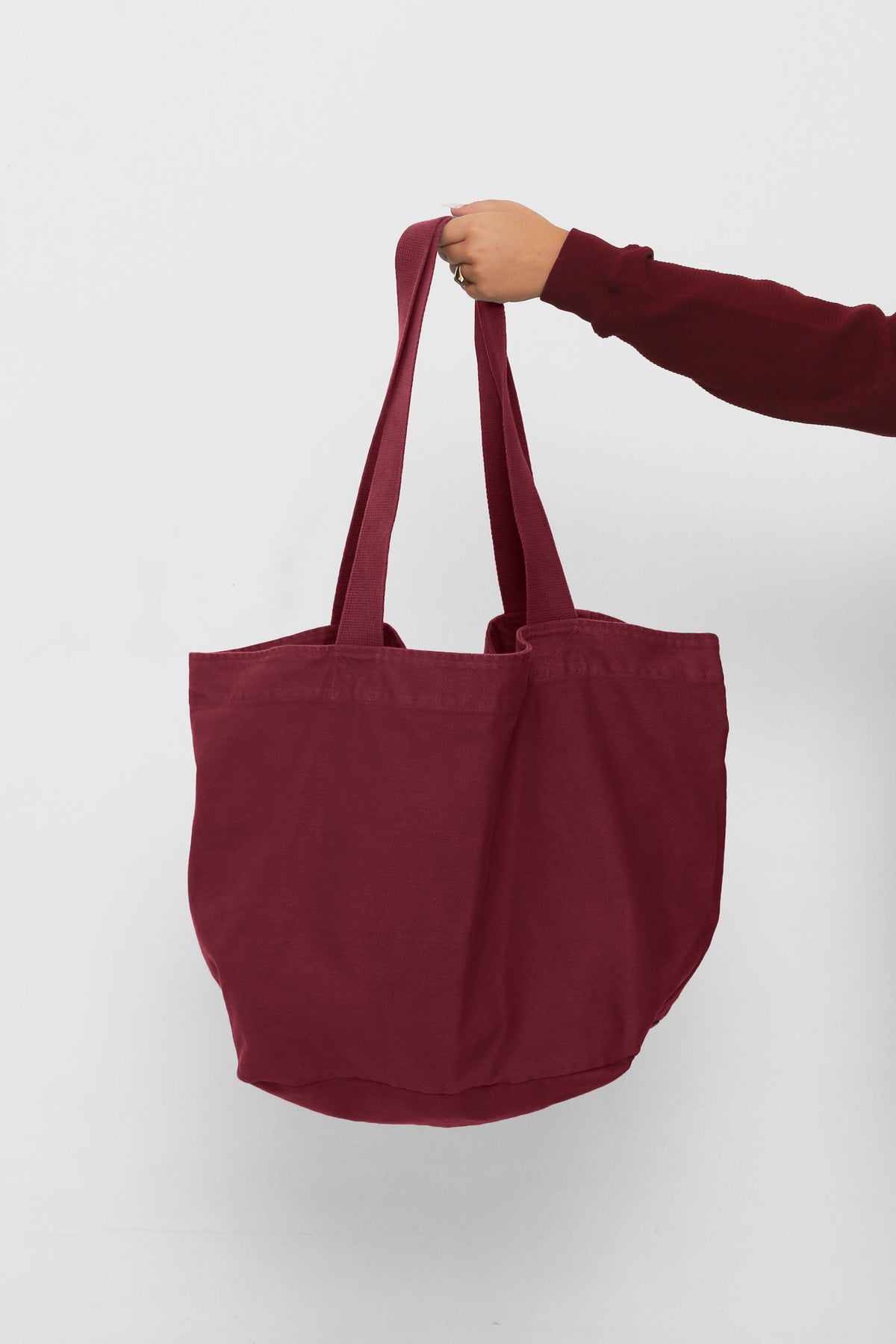 Big Tote in Garnet, held in a person's hand, showing gussets, depth and stitching.