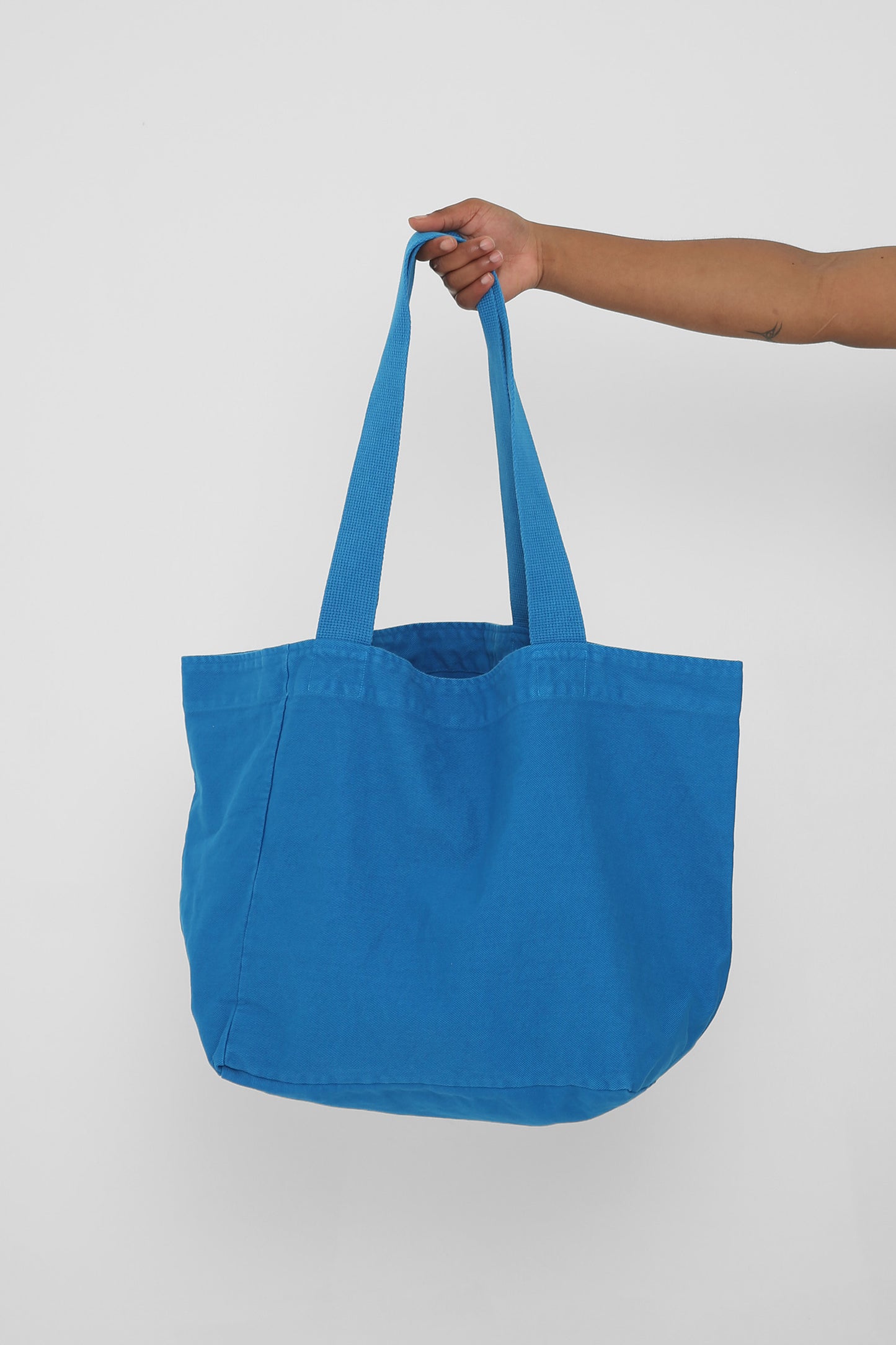 Big Tote in Malibu blue, held in a person's hand, showing gussets, depth and stitching.