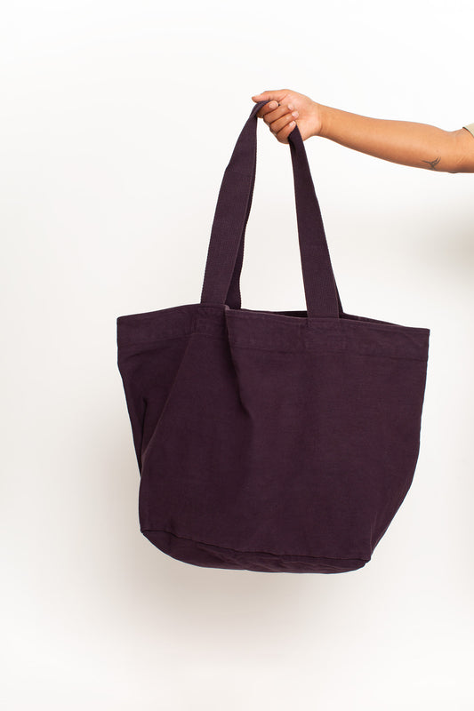 Big Tote in Mulberry dark purple, held in a person's hand, showing gussets, depth, stitching, and web straps.