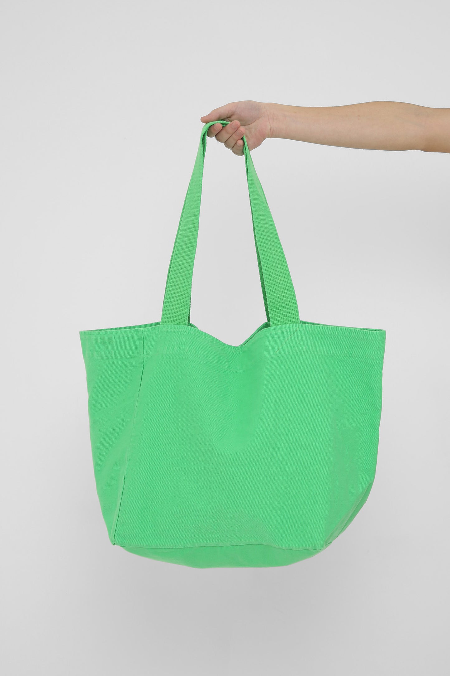 Big Tote in Nice Grass, held in a person's hand, showing gussets, depth and stitching.