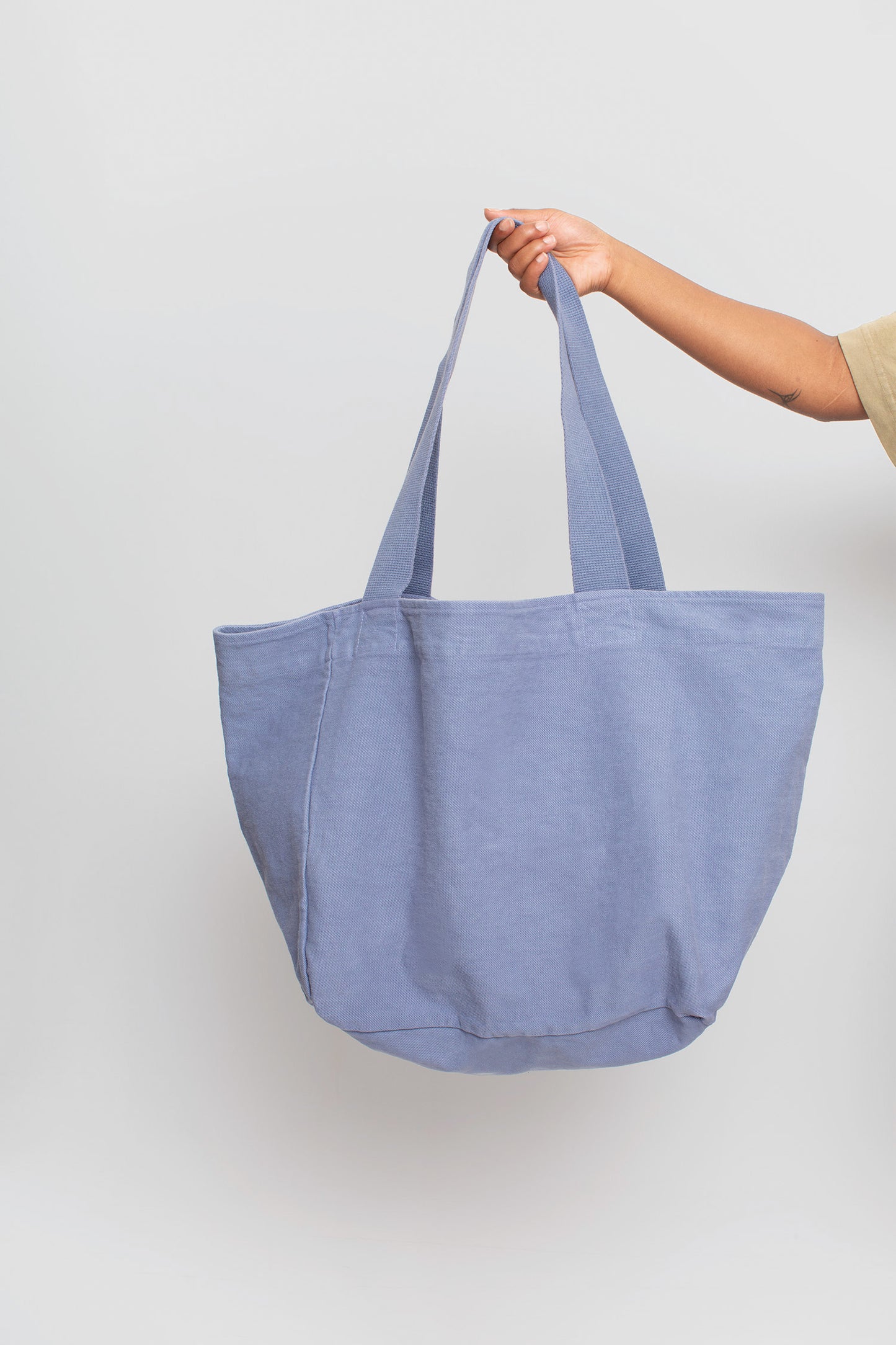 Big Tote in Periwinkle light blue-purple, held in a person's hand, showing gussets, depth, stitching, and web straps.