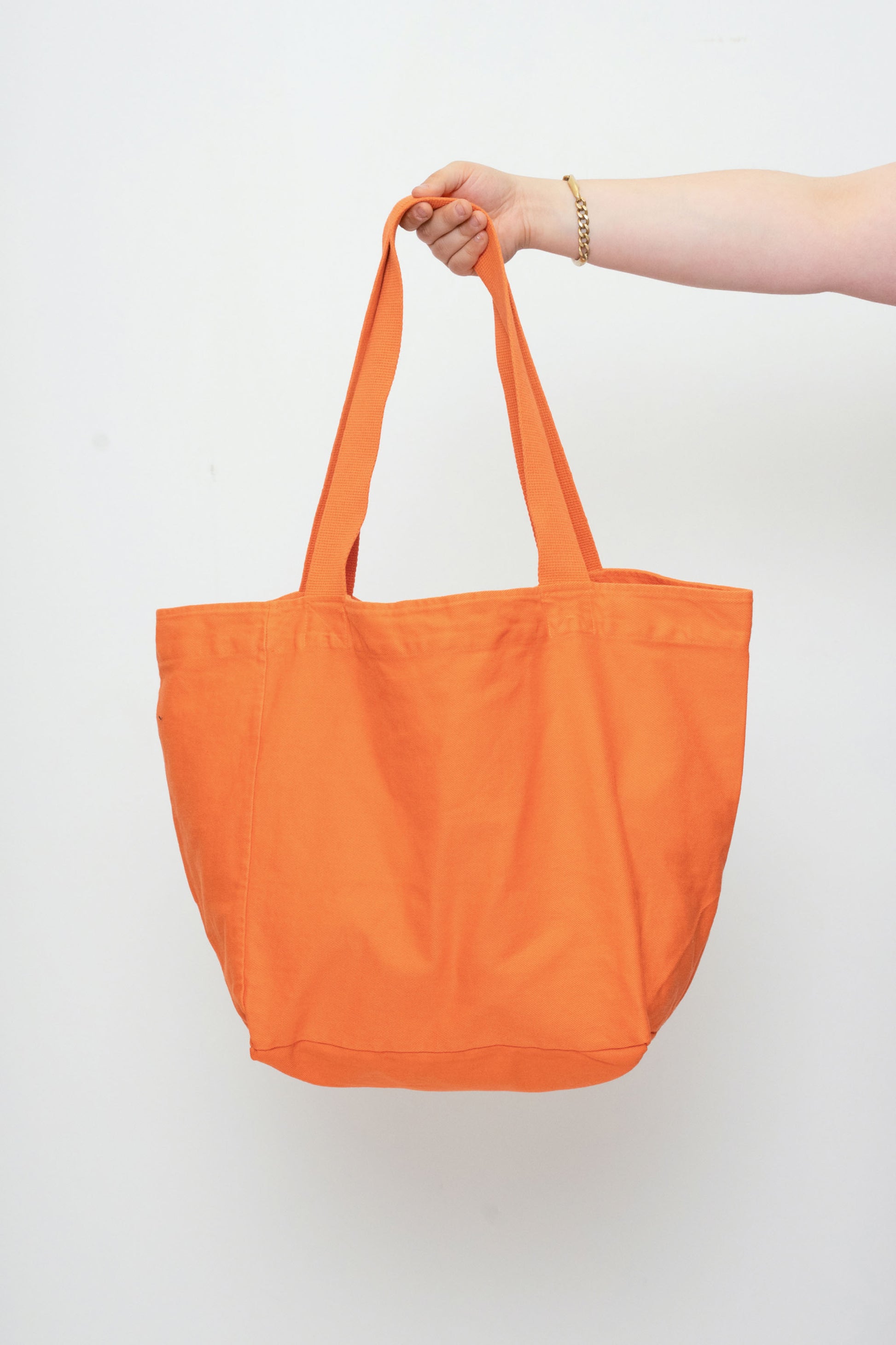 Big Tote in Persimmon orange, held in a person's hand, showing gussets, depth, stitching, and web straps.