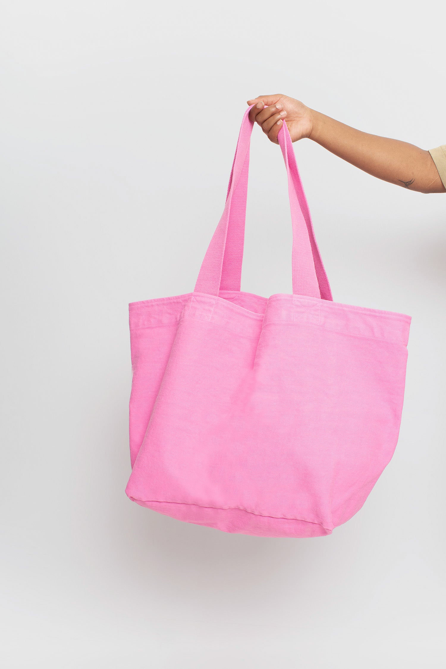 Big Tote in Pixie medium pink. Shows bottom and texture when hanging from a person's hand.