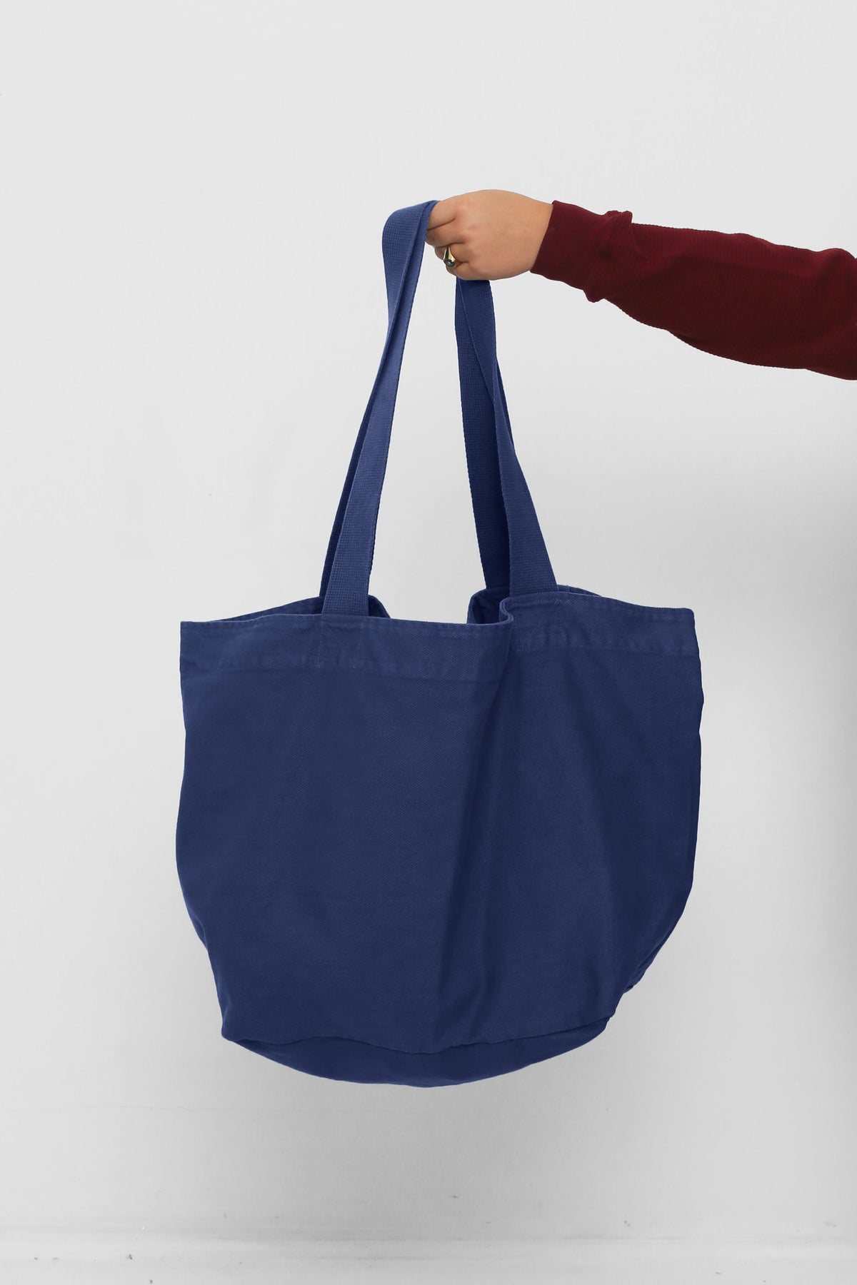 Big Tote in Washed Navy, held in a person's hand, showing gussets, depth and stitching.