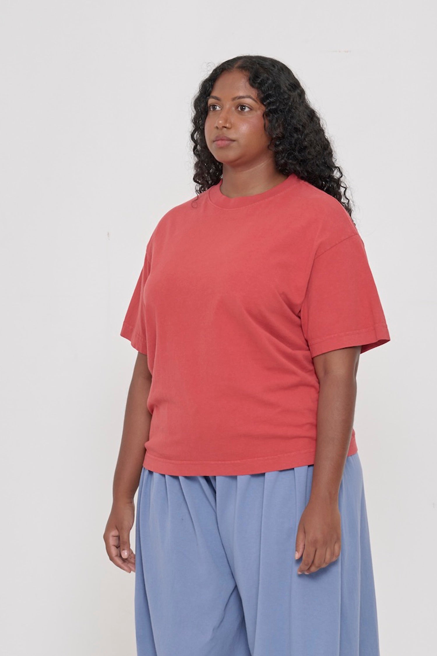 45-degree front view of a woman in a Cedar (orange red) Boxier Trash Tee showing wide short sleeves and no side seams.