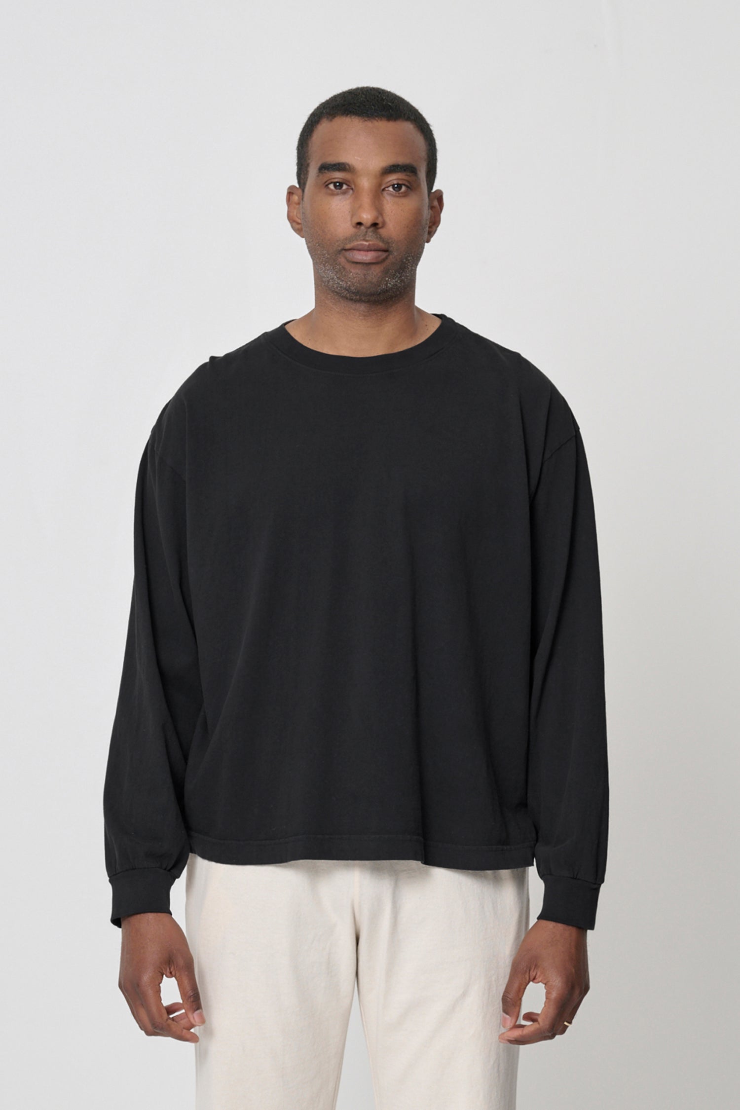 A 6'2" person wearing Black Long Sleeve Boxier Trash Tee in size XL. Their arms are straight down at their sides and shirt hem hits the middle of the hip. 