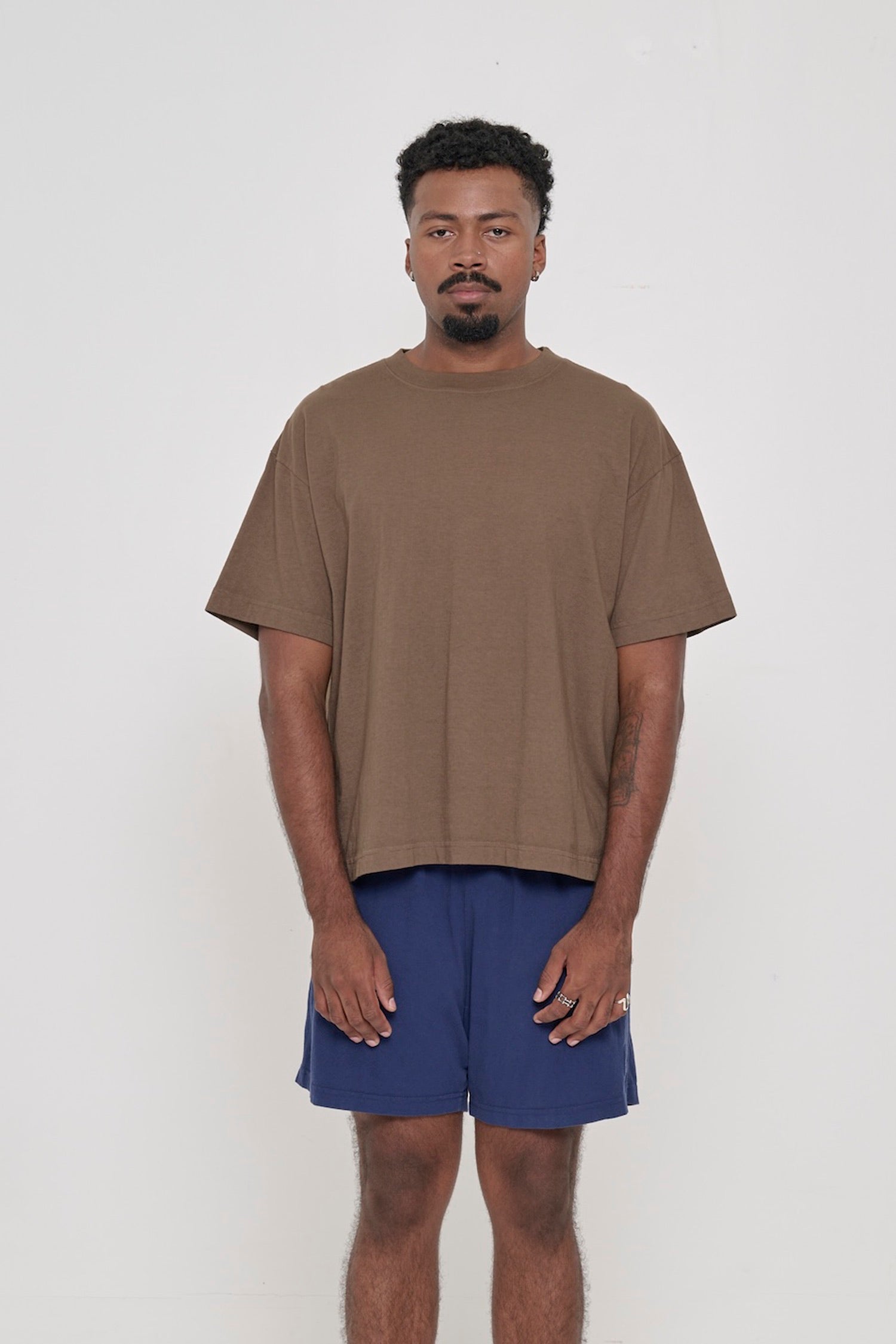 Front view of a man wearing Dry Soil brown Boxier Trash Tee. Bottom hem cropped to the mid upper hip.