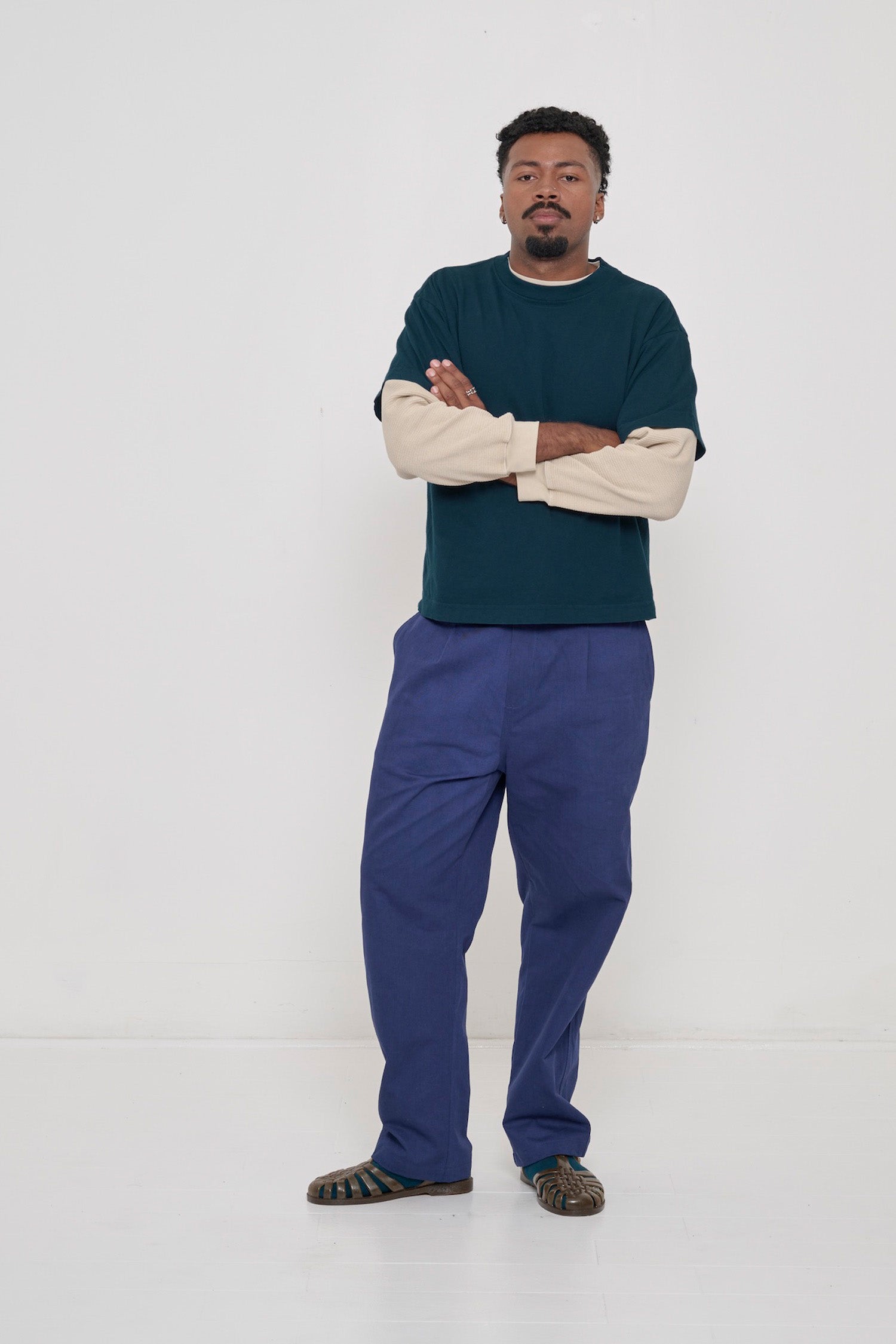 A man wearing Juniper dark teal Boxier Trash Tee worn over Oat Thermal Long Sleeve Boxier Trash Tee. 