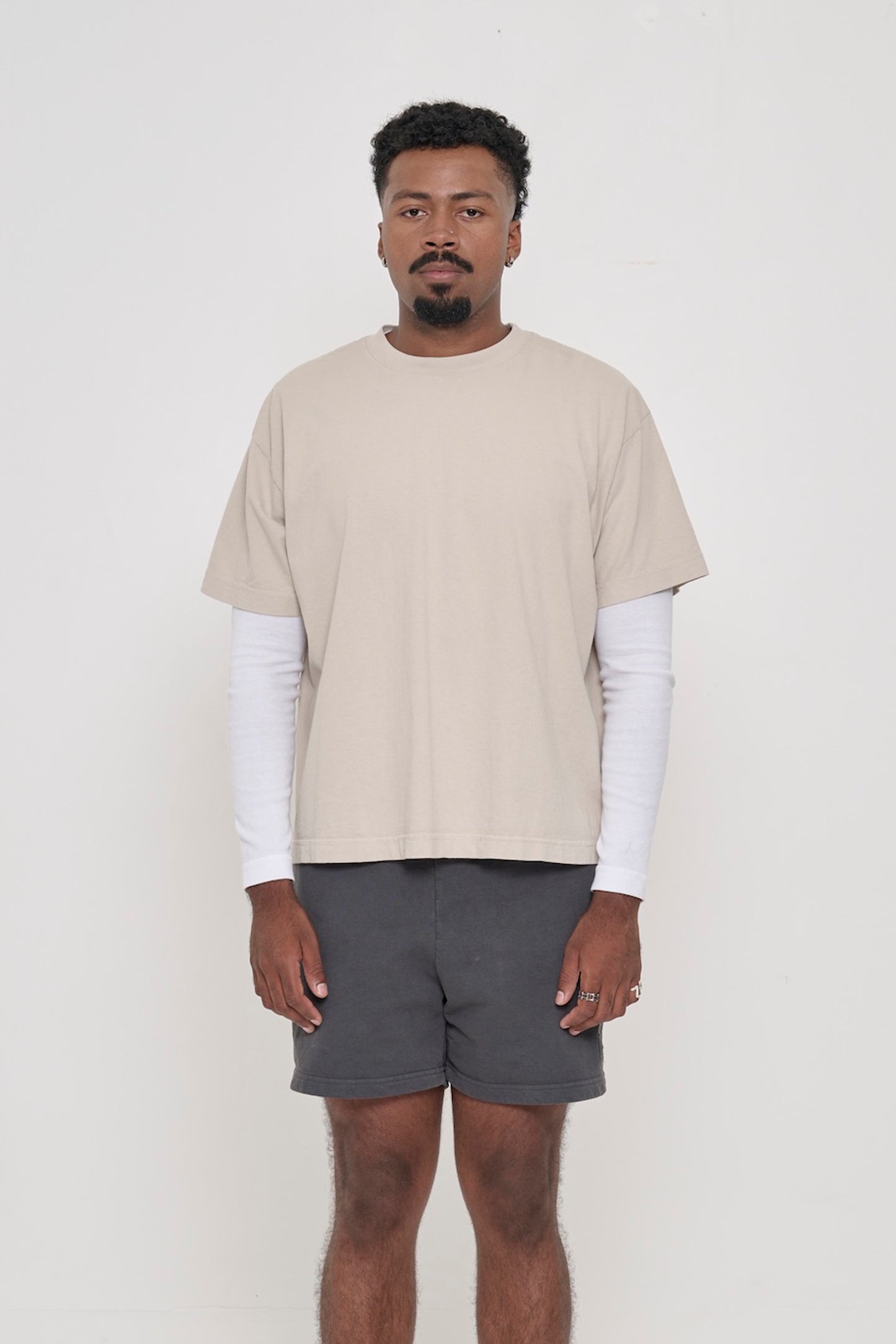 Front view of a man wearing Oat beige Boxier Trash Tee. Bottom hem cropped to the mid upper hip.