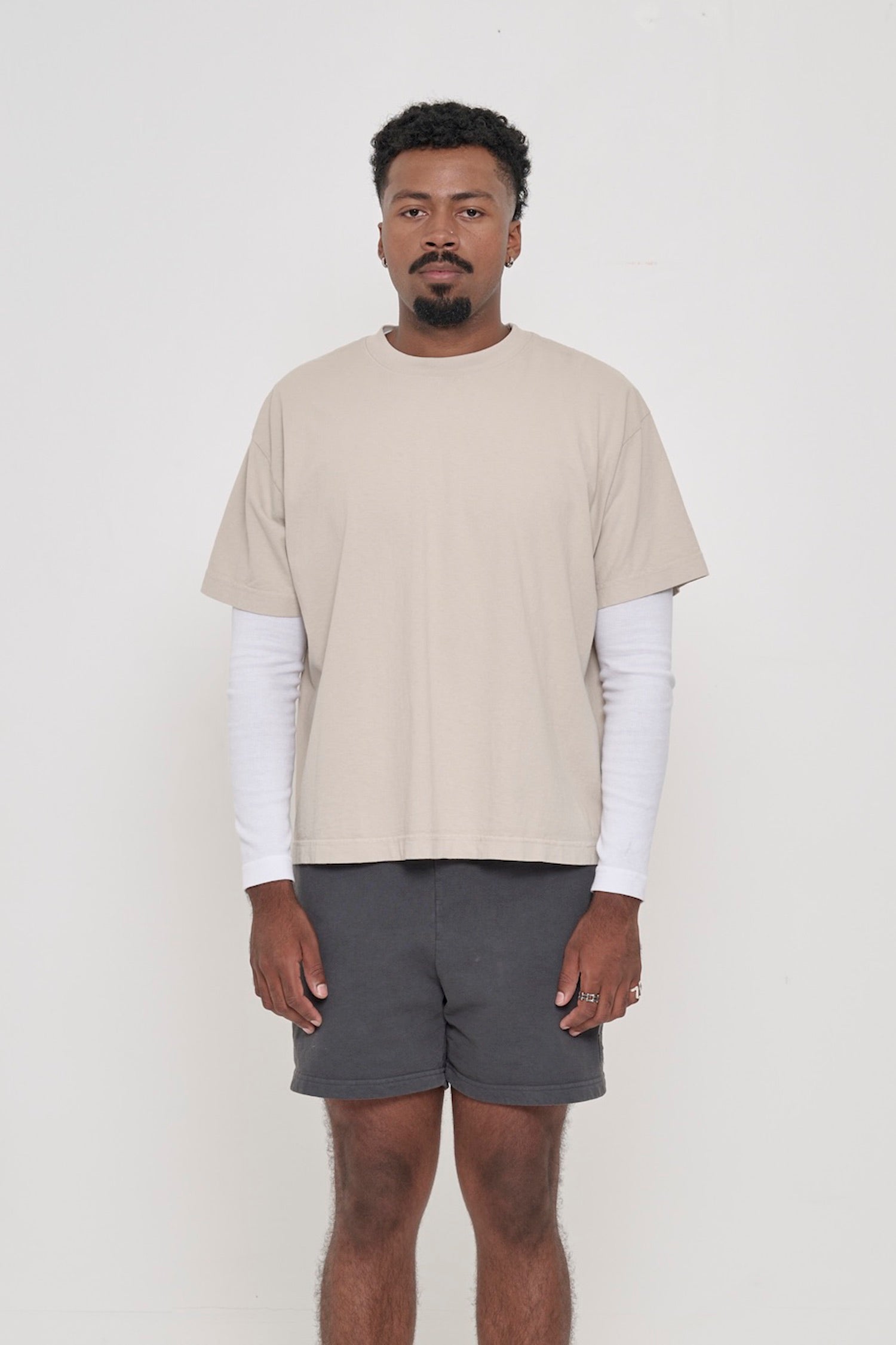 Front view of a man wearing Oat beige Boxier Trash Tee. Bottom hem cropped to the mid upper hip.