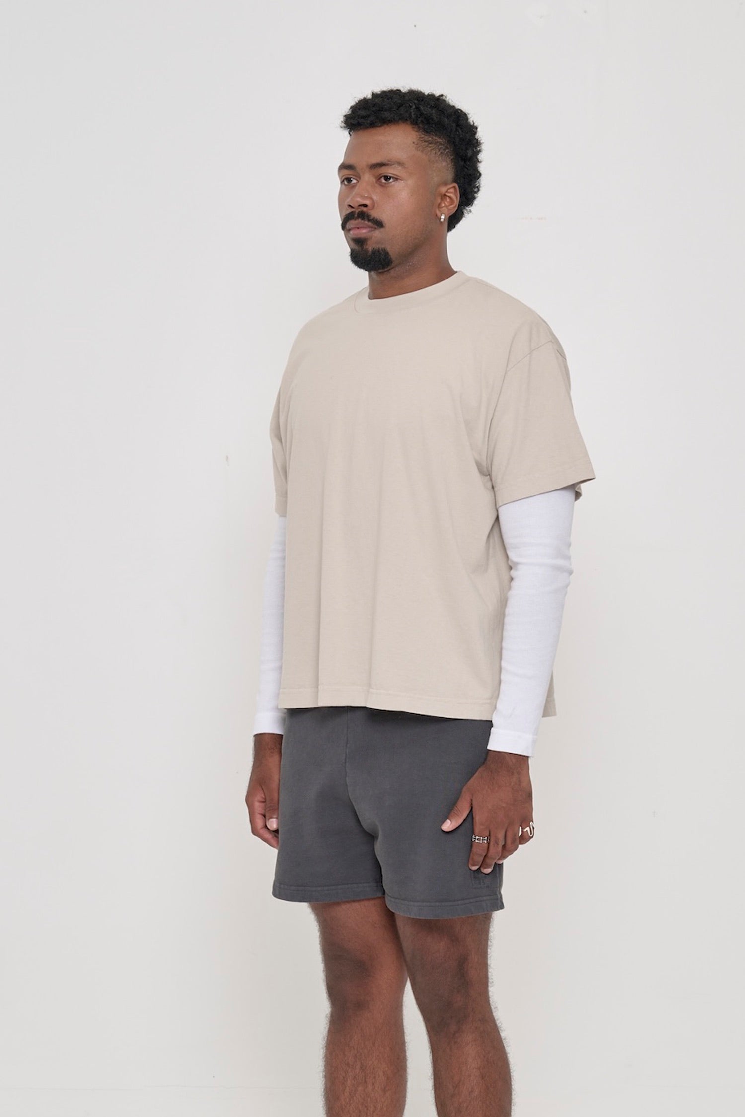 3/4 front view of person wearing Oat beige Boxier Trash Tee with no side seams and wider than classic short sleeves. 
