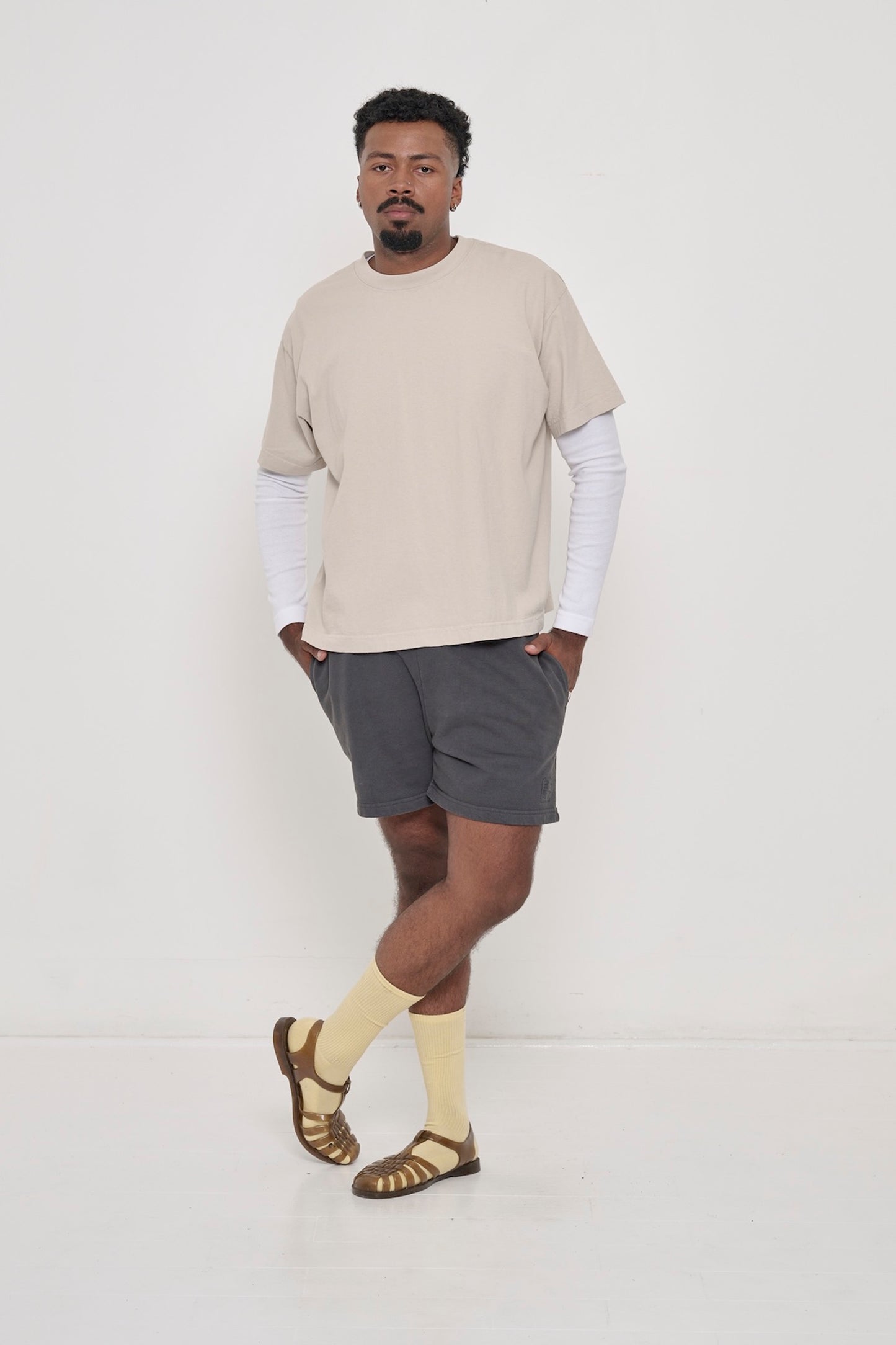 Man wearing Oat beige Boxier Trash Tee layered over Rib Long Sleeve in White and Slate Everyday Shorts. 
