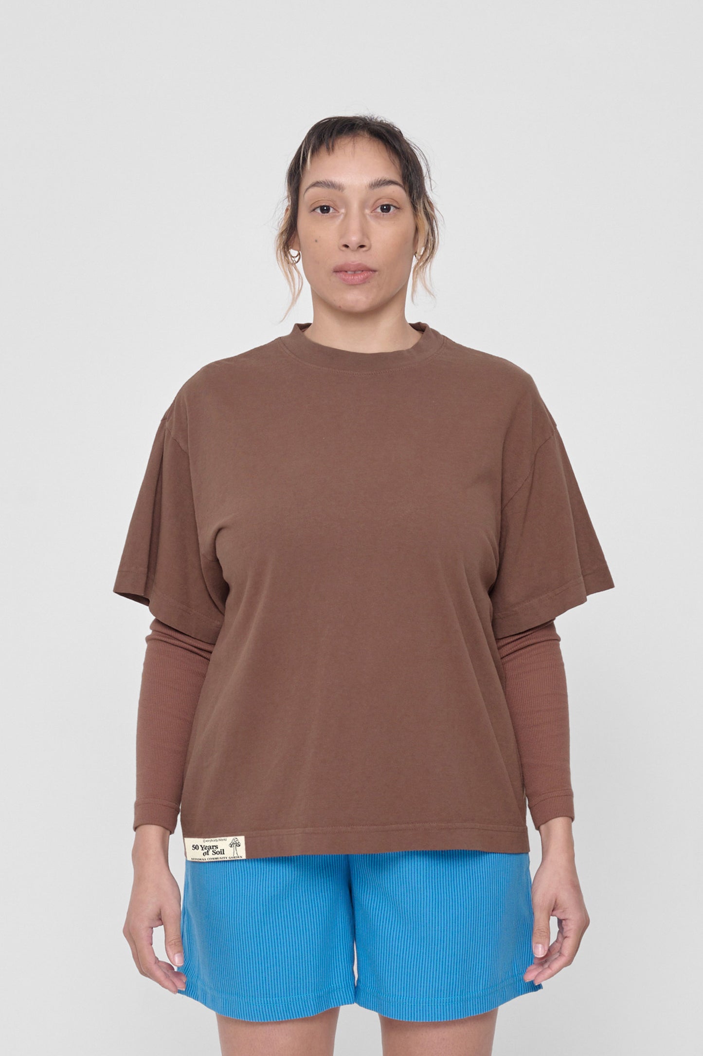 A 5'4" woman in a size M Potting Soil Boxier Trash Tee. Hem at her lower hip.