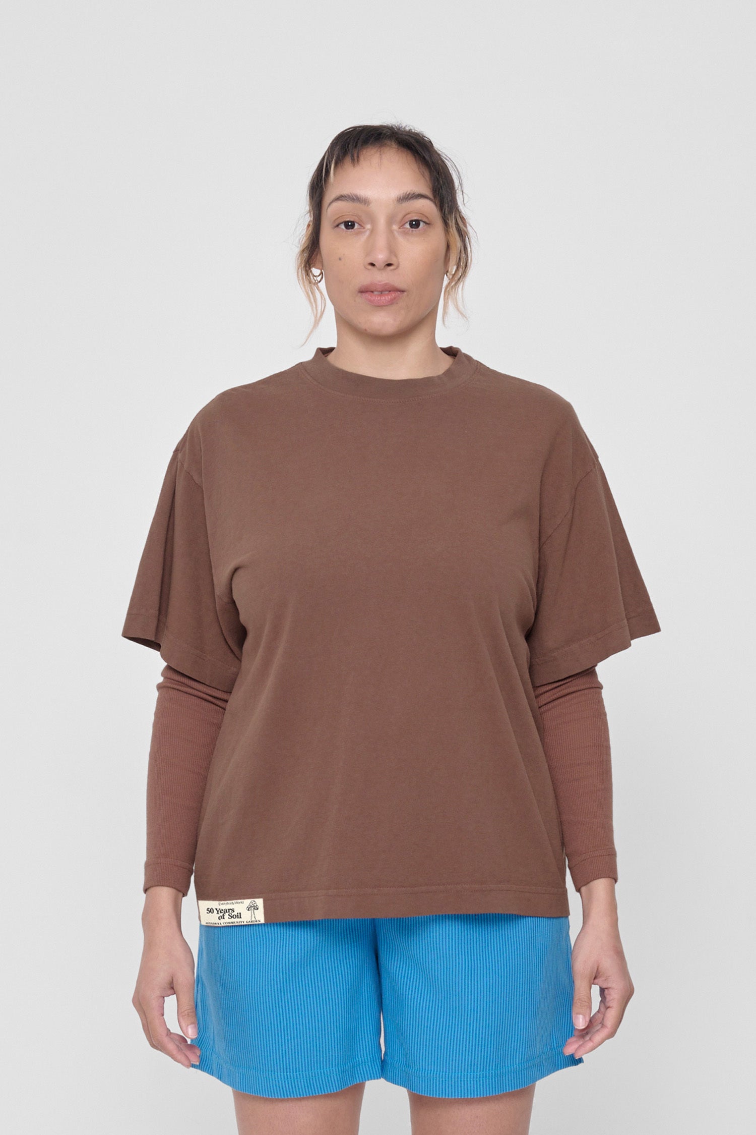 A 5'4" woman in a size M Potting Soil Boxier Trash Tee. Hem at her lower hip.