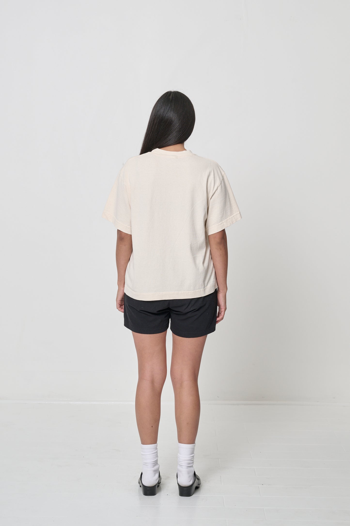 Back view: A woman wearing a Scour Boxier Trash Tee with Black Everyday Shorts showing the relaxed boxy fit.