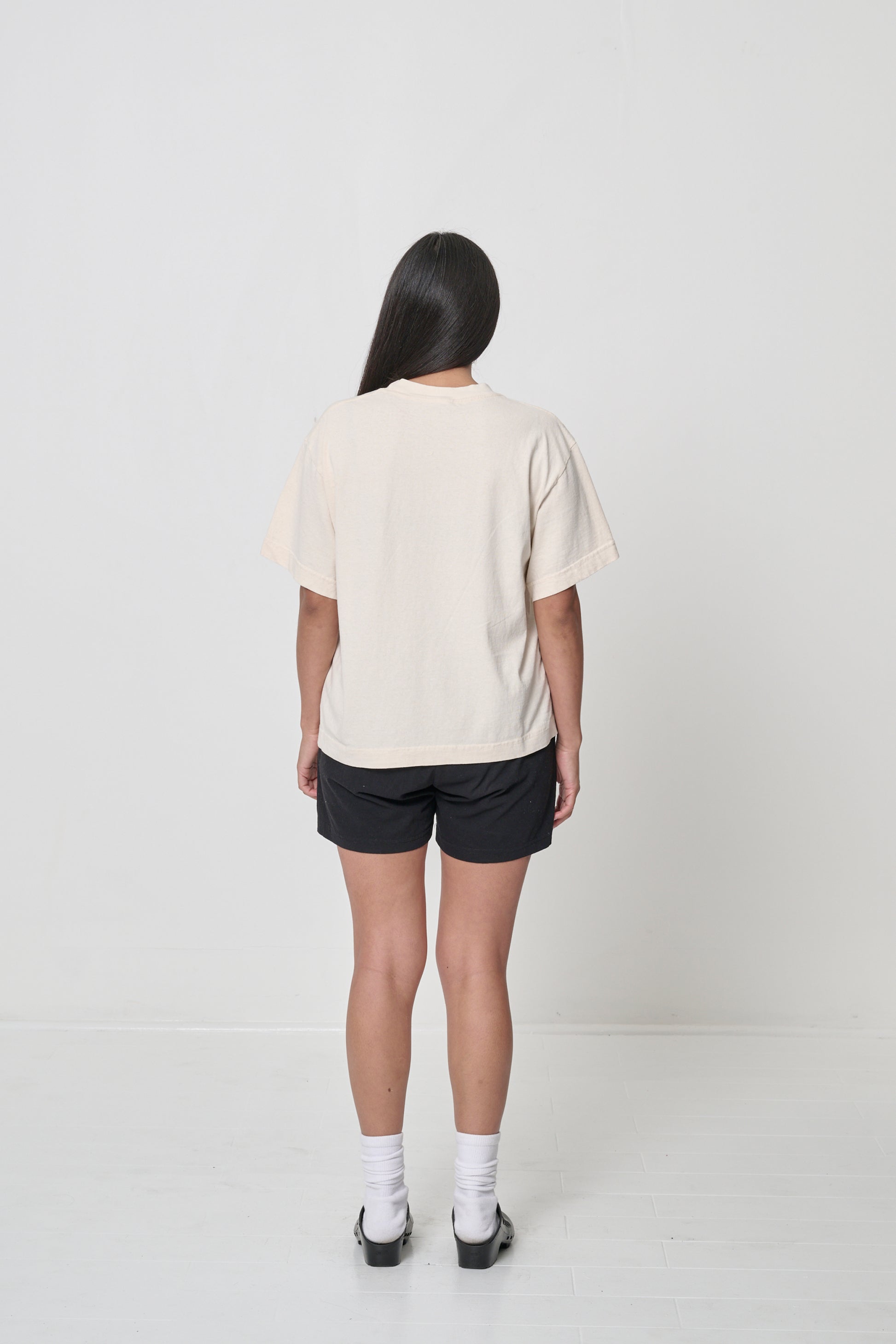 Back view: A woman wearing a Scour Boxier Trash Tee with Black Everyday Shorts showing the relaxed boxy fit.