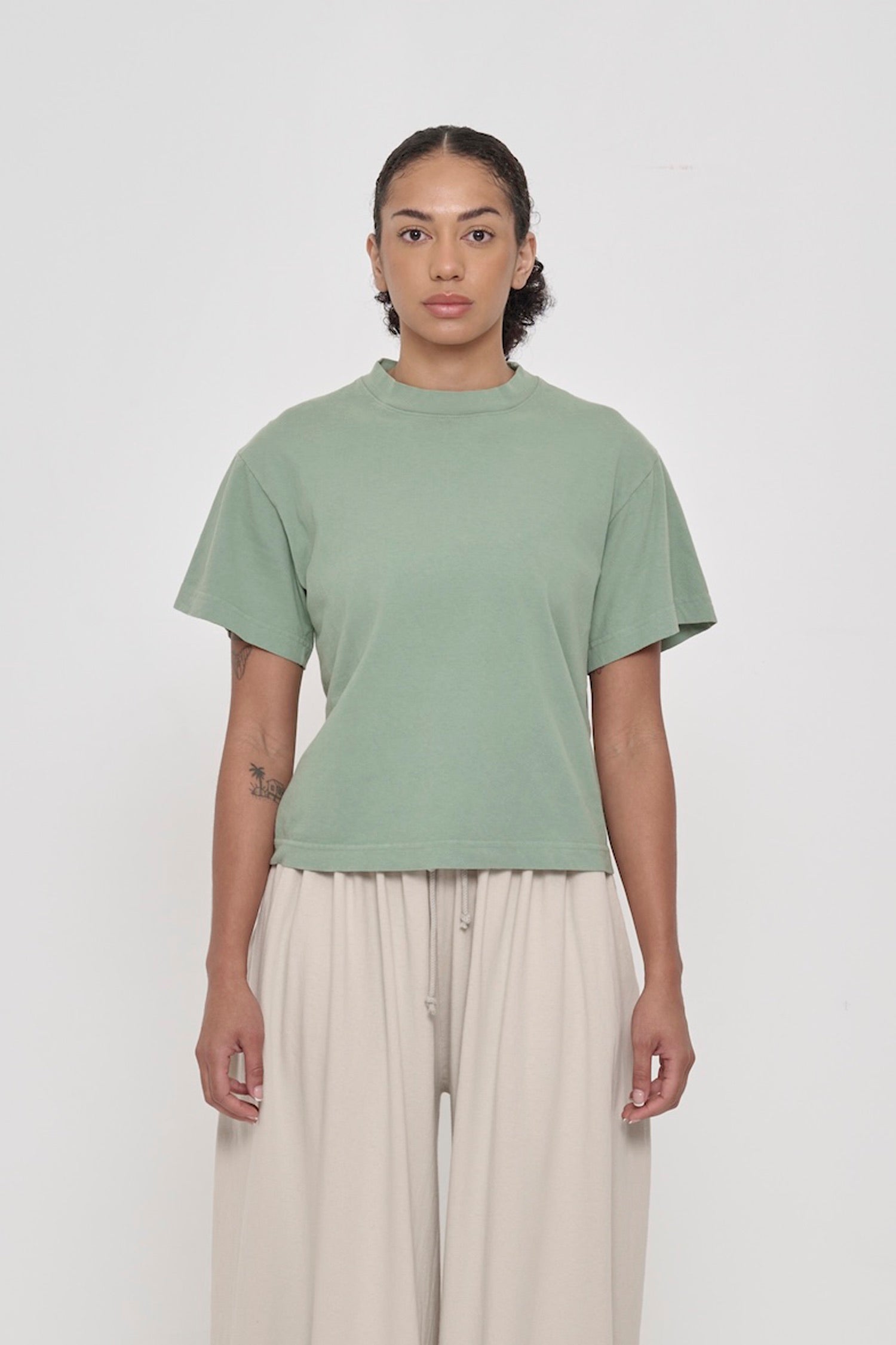 Front view of a woman wearing Wasabi light green Boxier Trash Tee. Bottom hem cropped to the mid upper hip.