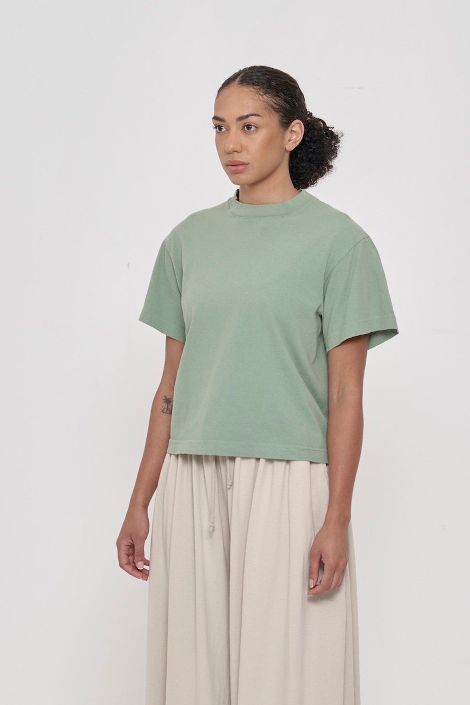 3/4 front view of person wearing Wasabi Boxier Trash Tee with no side seams and wider than classic short sleeves. 