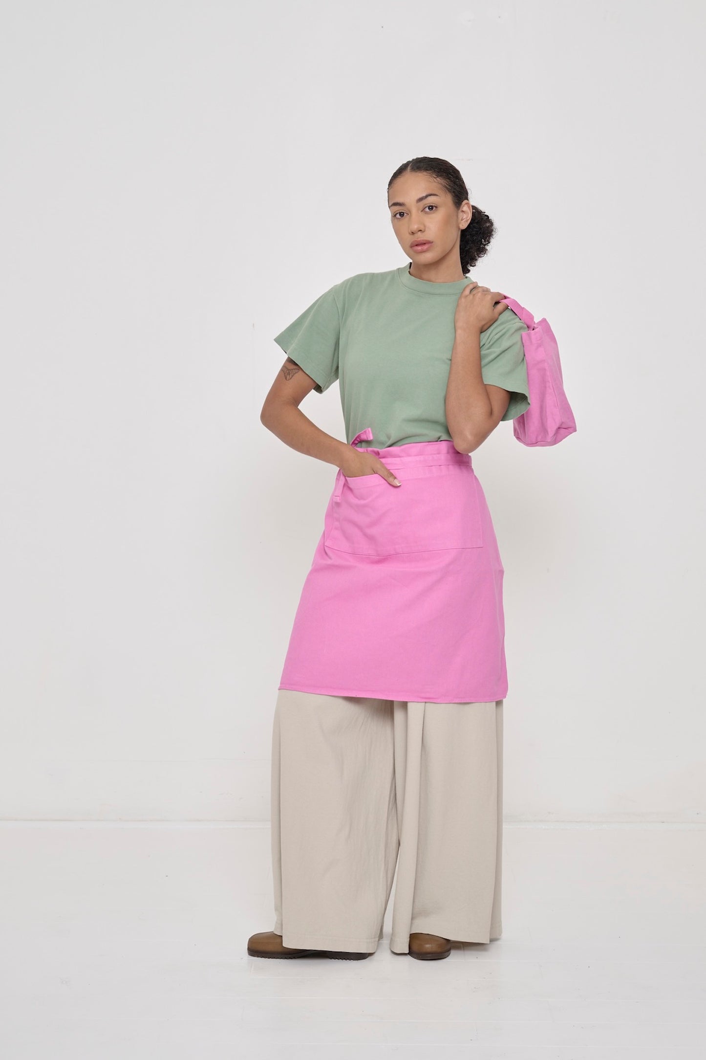 Woman wearing Wasabi light green Boxier Trash Tee with Pixie Adjustable Apron folded half way and Pixie Loop Tote.