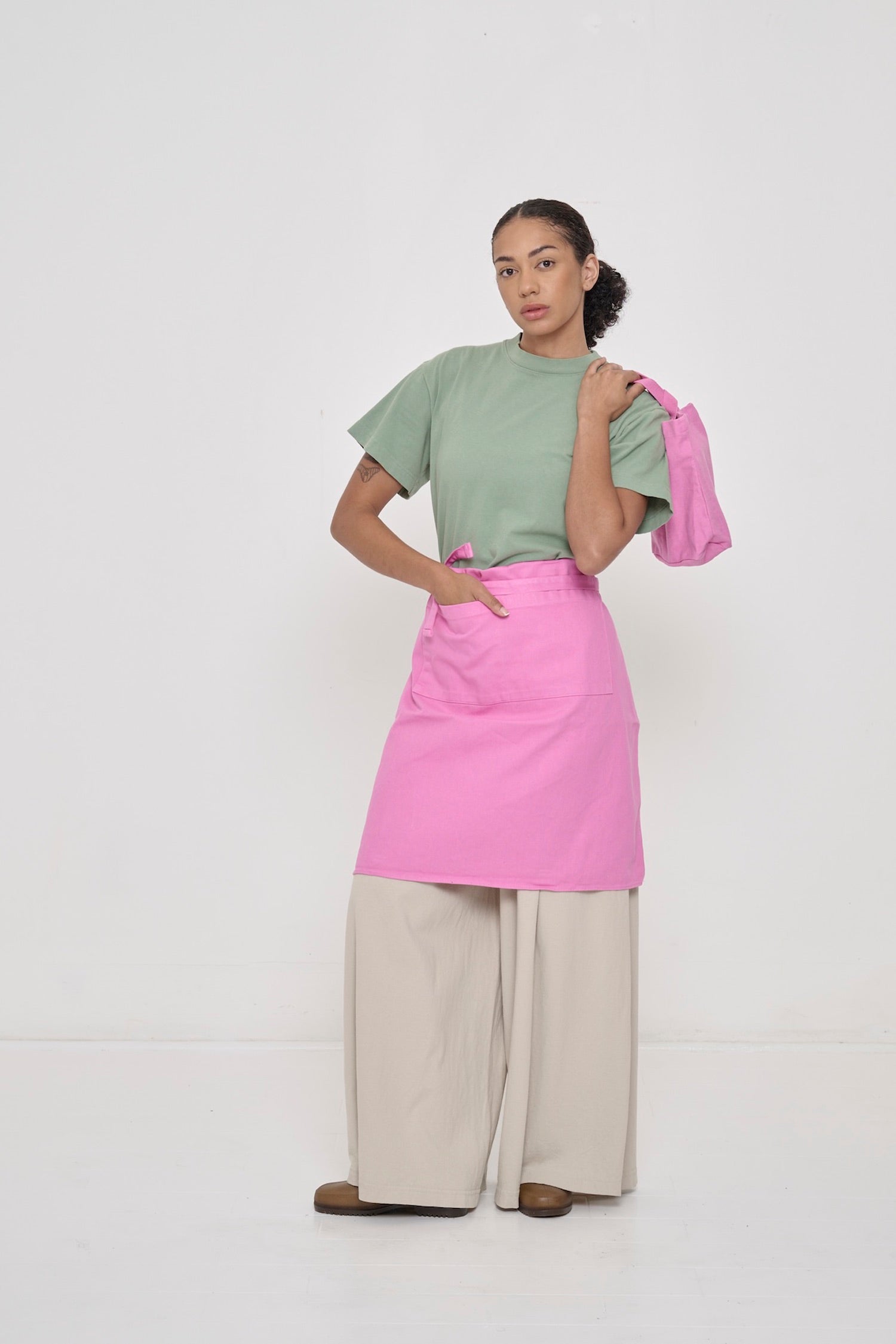 Woman wearing Wasabi light green Boxier Trash Tee with Pixie Adjustable Apron folded half way and Pixie Loop Tote.