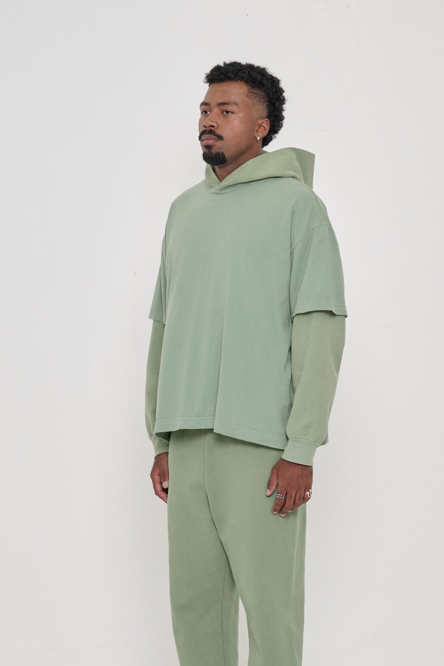 3/4 front view of person wearing Wasabi green Boxier Trash Tee with no side seams and wider than classic short sleeves. 
