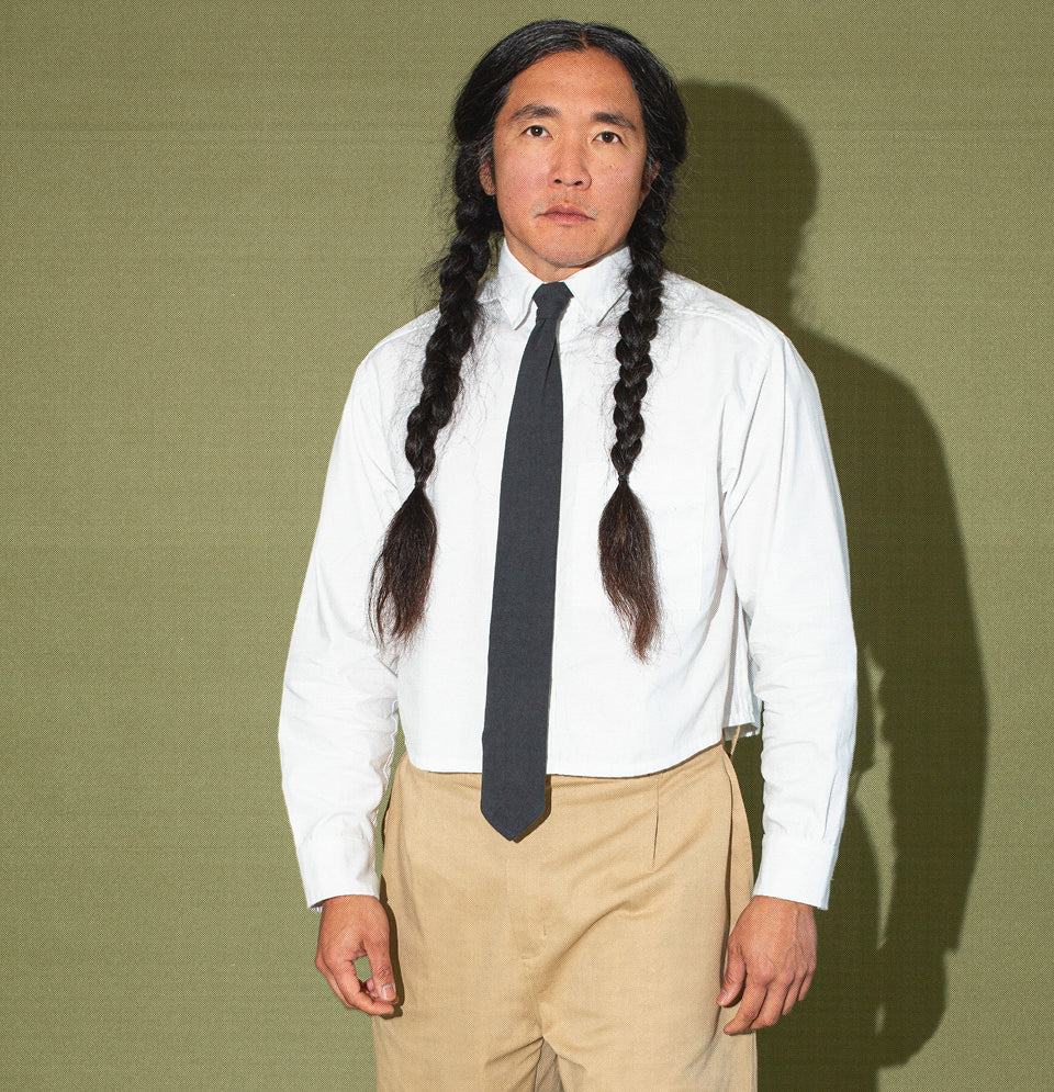Man wearing Peach Fuzz Cropped Button-Up in White with a Slate Trash Tie, and Life Uniform Pants in Sandstorm.