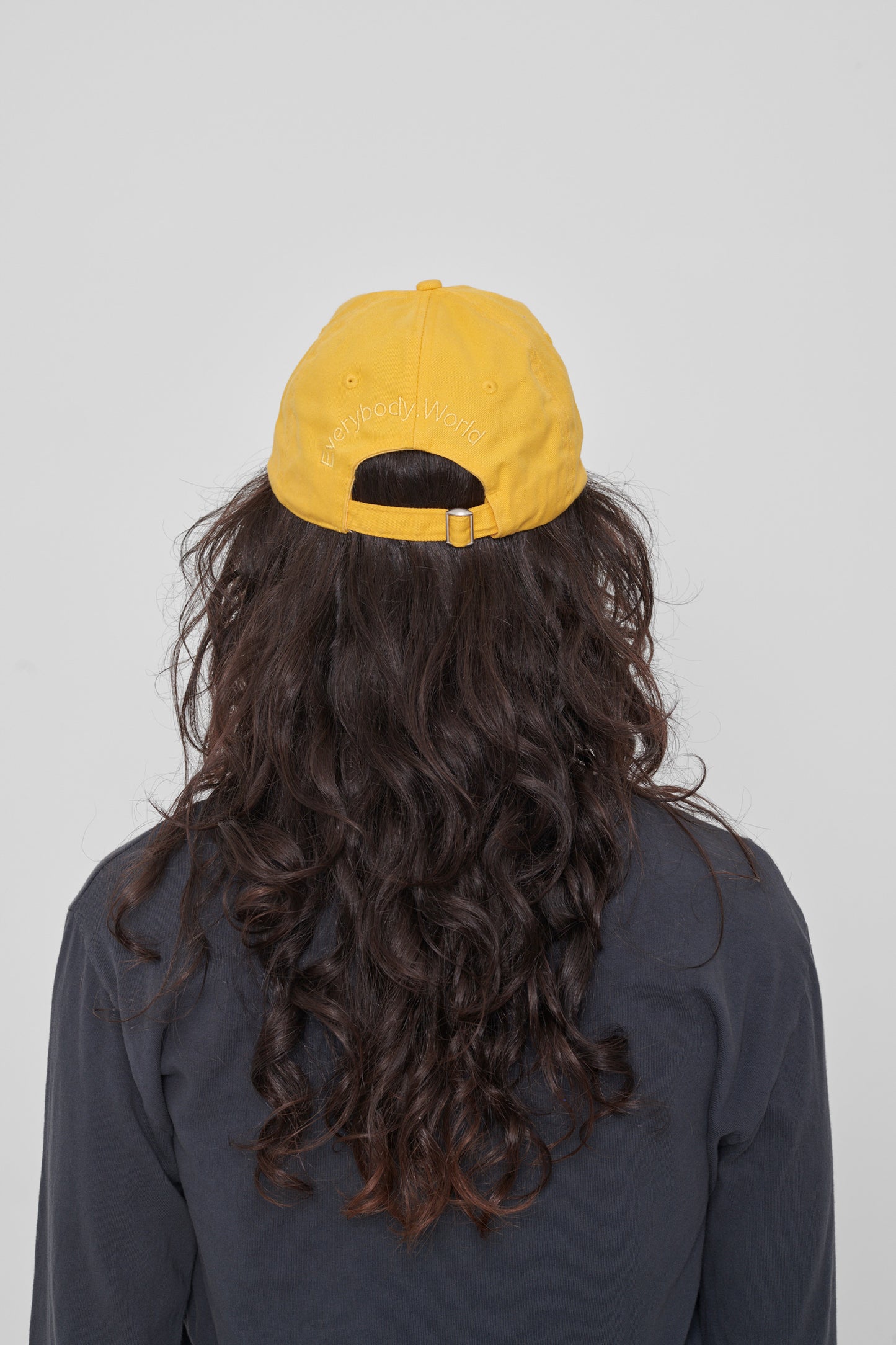 Back view on a woman: 'Everybody,World' embroidered in an arc above the adjustable closure. 