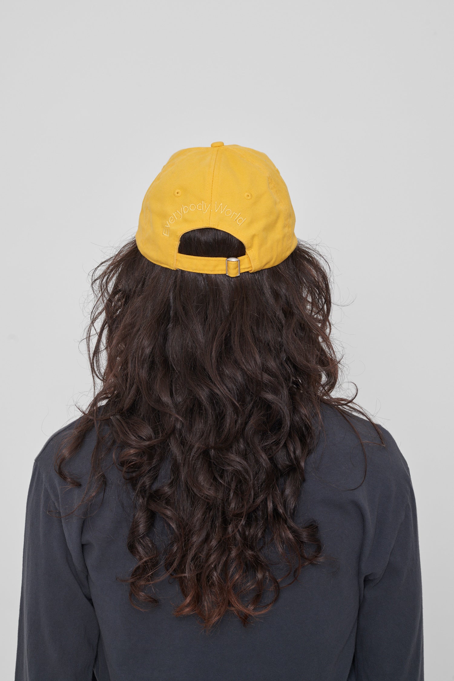 Back view on a woman: 'Everybody,World' embroidered in an arc above the adjustable closure. 