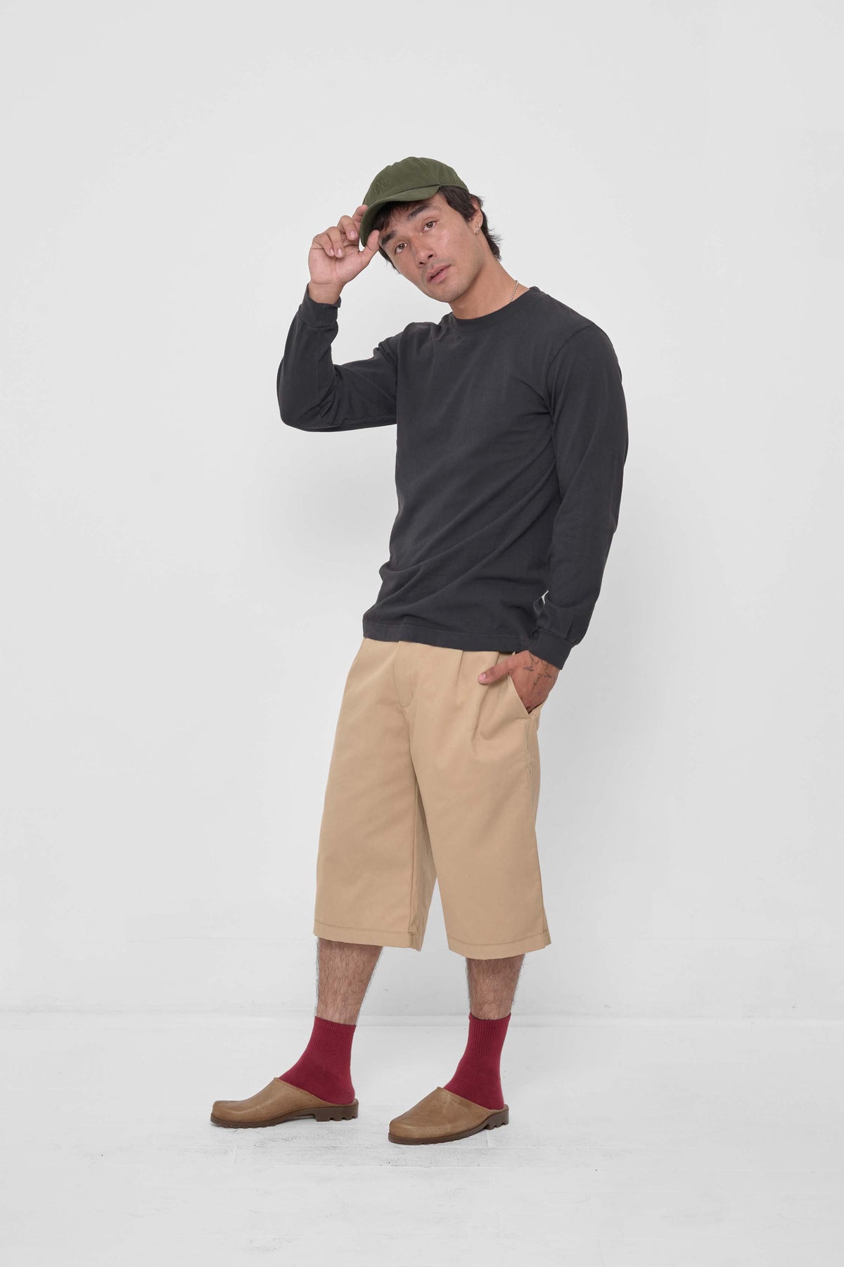 Bucky Logo Cap in Olive - front full body view of model, styled with Slate Long Sleeve Trash Tee, Sand Storm Bermuda Shorts, Garnet Squishy Socks, and Plasticana Mules.