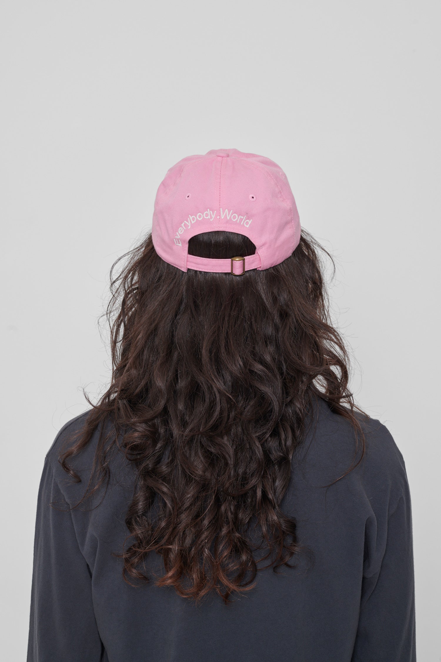 Back view on a woman: 'Everybody,World' embroidered in an arc above the adjustable closure. 