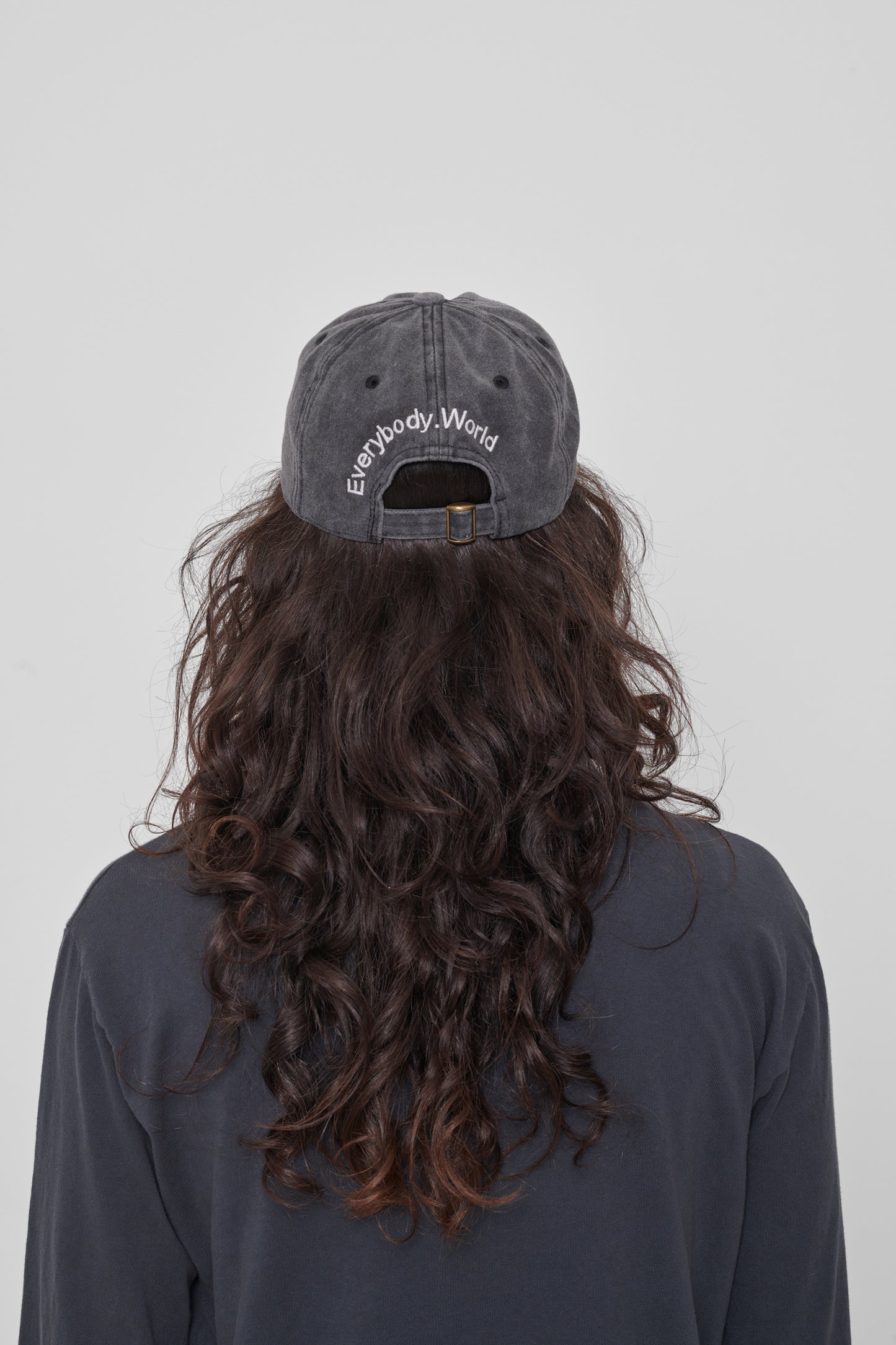 Back view on a woman: 'Everybody,World' embroidered in an arc above the adjustable closure. 