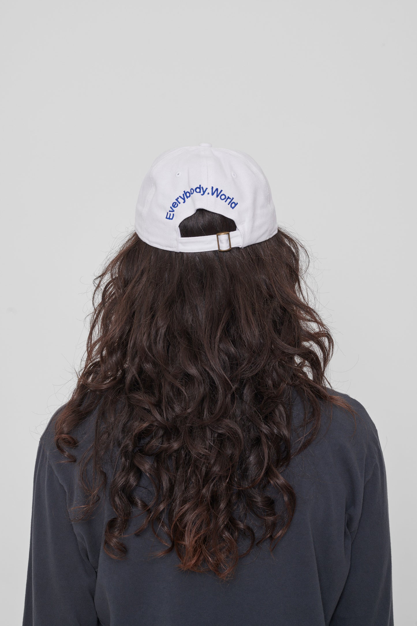 Back view on a woman: 'Everybody,World' embroidered in an arc above the adjustable closure. 
