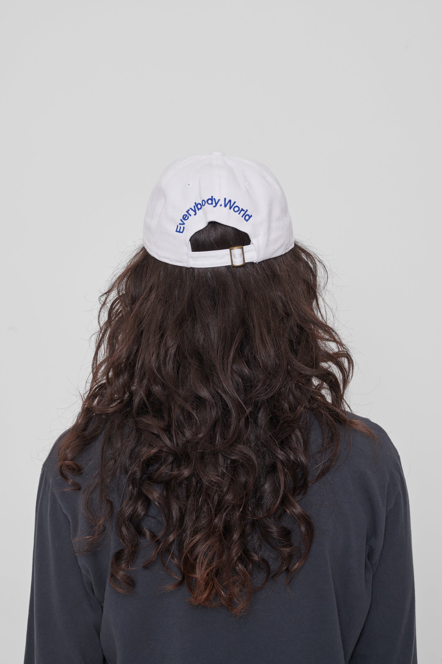 Back view on a woman: 'Everybody,World' embroidered in an arc above the adjustable closure. 