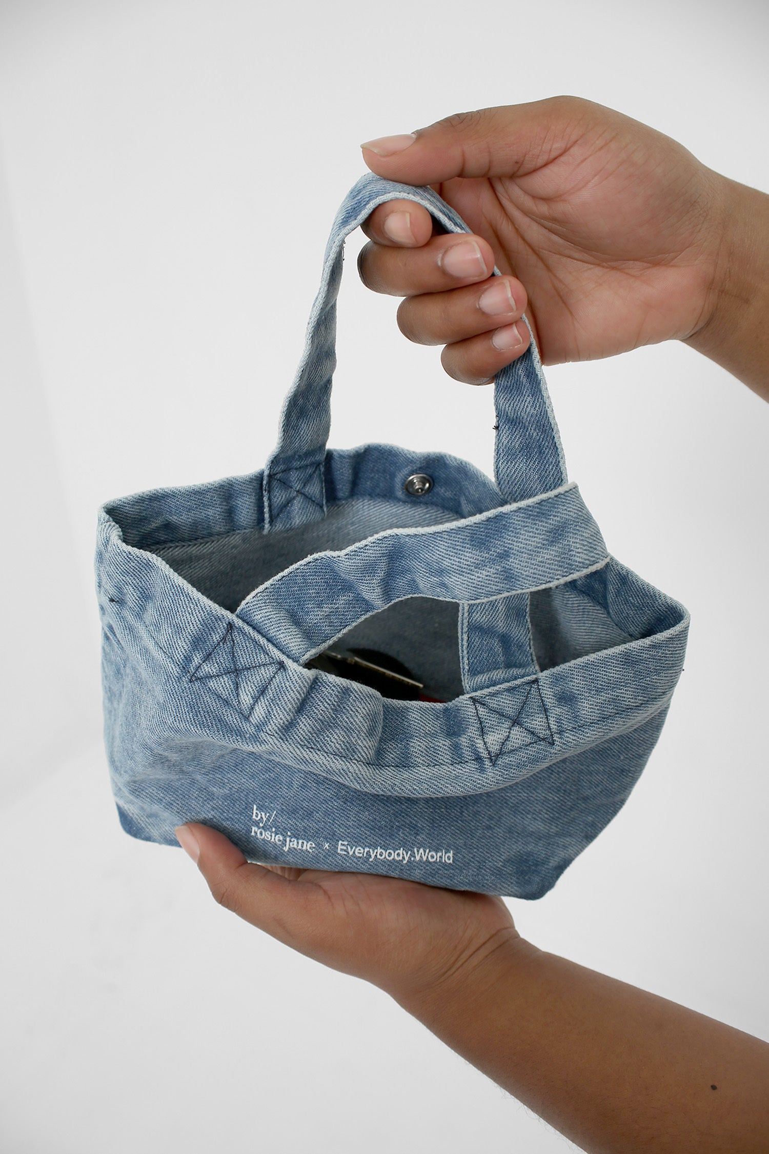 Overhead view with bag open to show contents: a wallet, a phone and sunglasses.