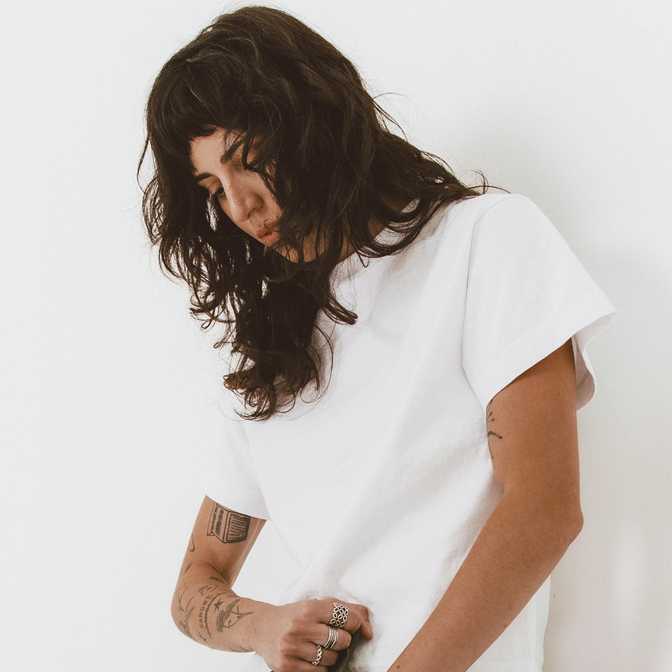 Woman looking down and wearing a Boxier Trash Tee in White against a plain background.