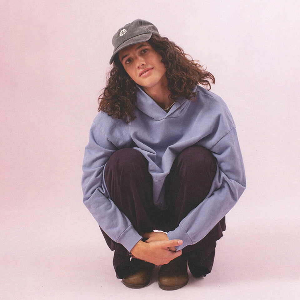 Person sitting wearing Trash Hoodie in Periwinkle, Tubular Pants in Mulberry and Bucky Logo Cap in Slate.