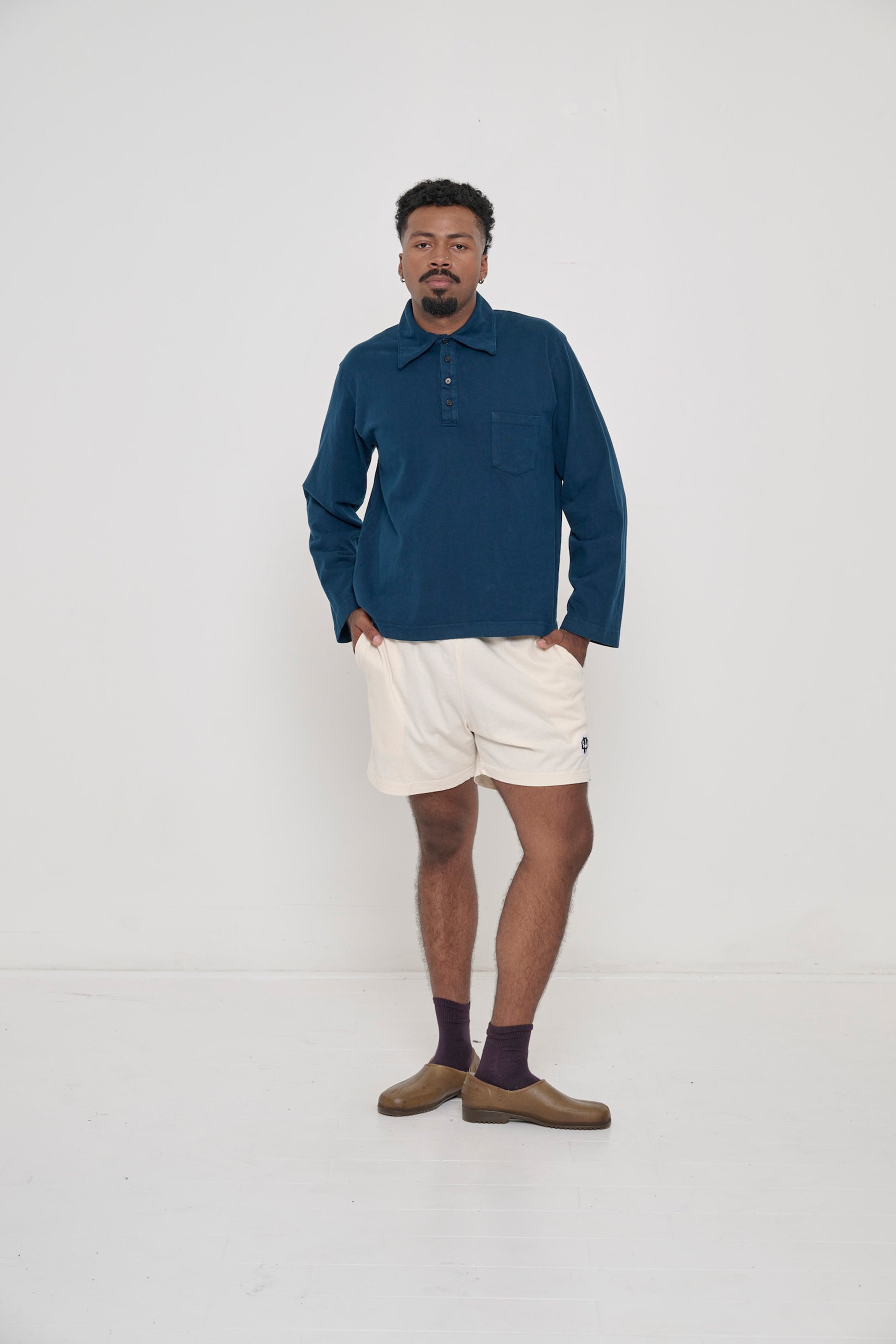 A person in a Juniper Rugby Trash Polo and Scour Everyday Shorts. Left knee popped to the side, showing inseam.