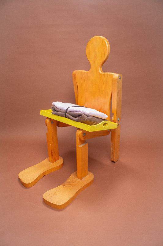 Wooden mannequin chair with Lavender and Soil sweatshirts folded on its lap.