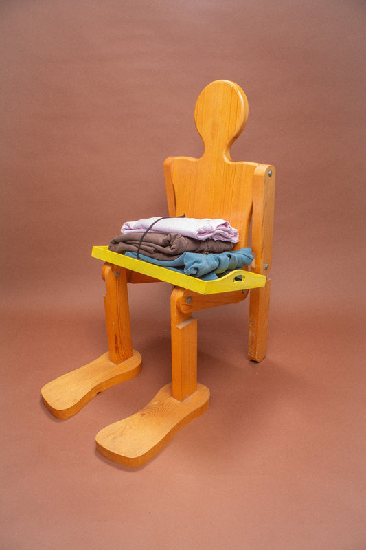 Wooden mannequin chair with Lavender and Soil sweatshirts folded on its lap.