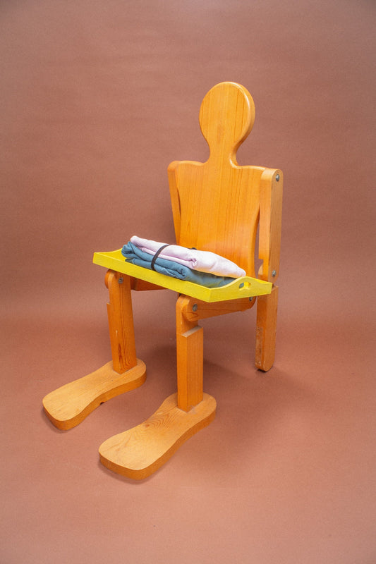 Wooden mannequin chair with pink and blue folded sweatshirts on its lap.